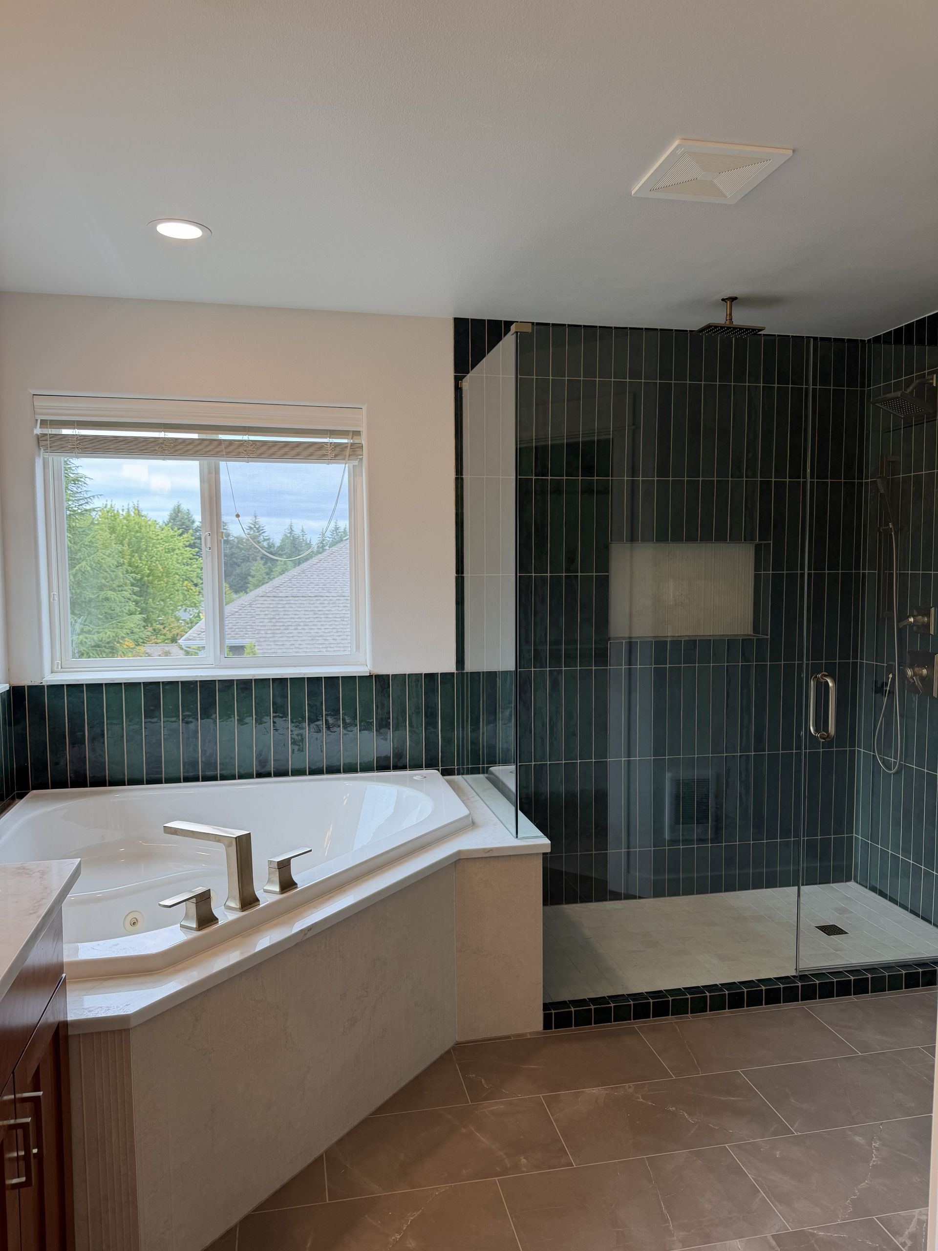Bathroom with white tub, black tile shower, and window letting in daylight.