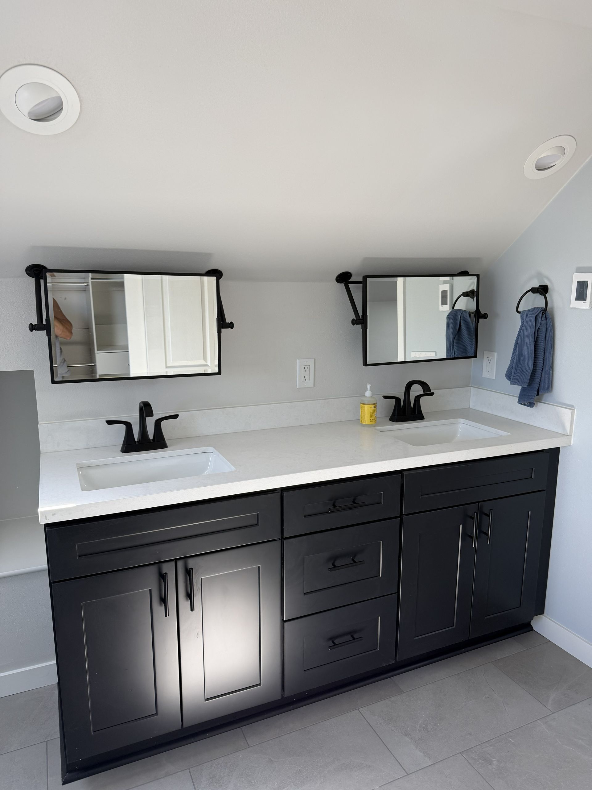 Modern bathroom vanity with double sinks, black cabinets, white countertop, and mirrors