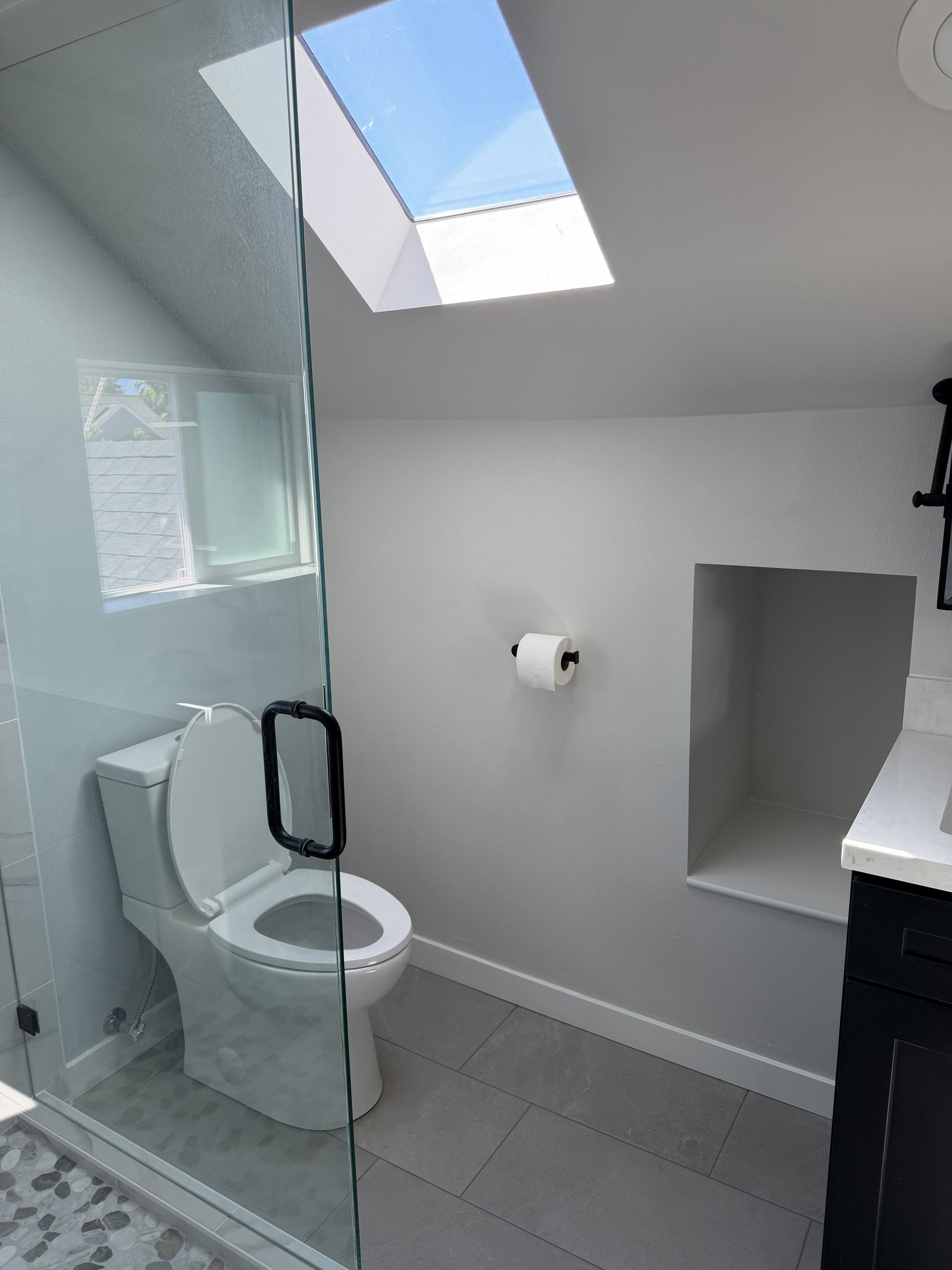 Modern bathroom with glass shower, toilet, skylight, and white walls