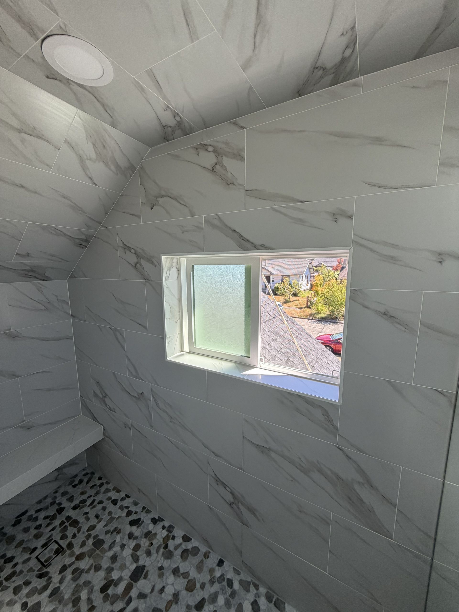 Small tiled bathroom with a window, white walls, and a pebble-pattern floor.