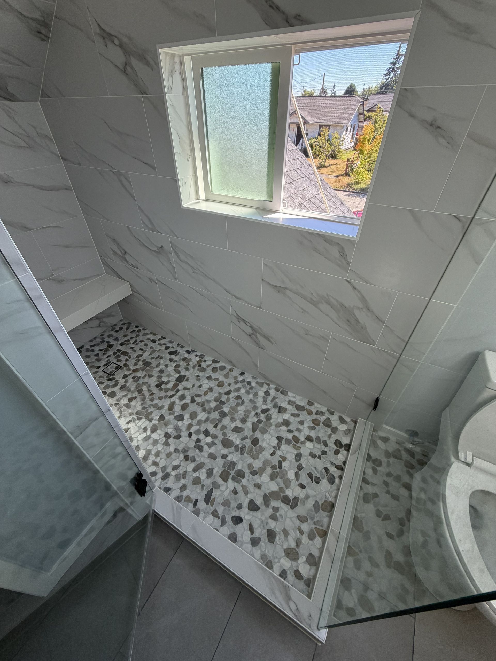 Small tiled bathroom with shower stall, window, and a toilet visible on the right.