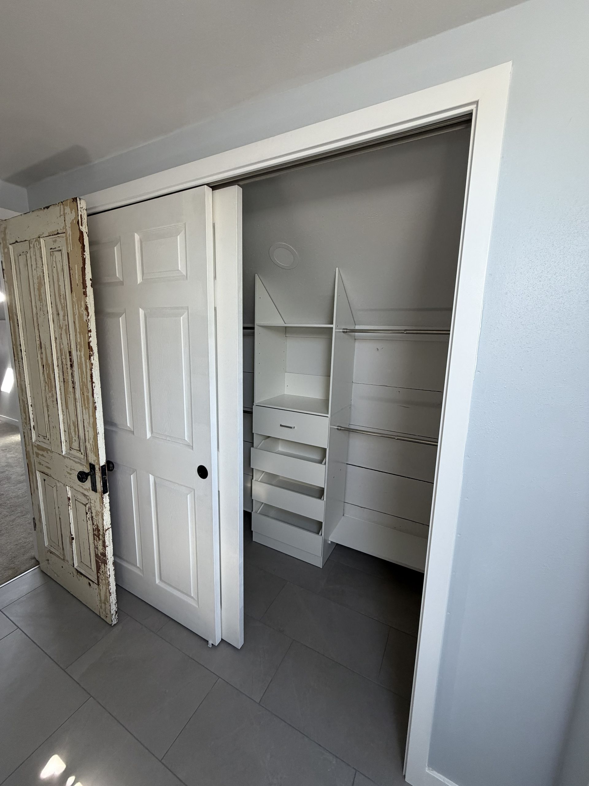 Open closet with white shelves, hanging rod, and double doors in a tiled room.