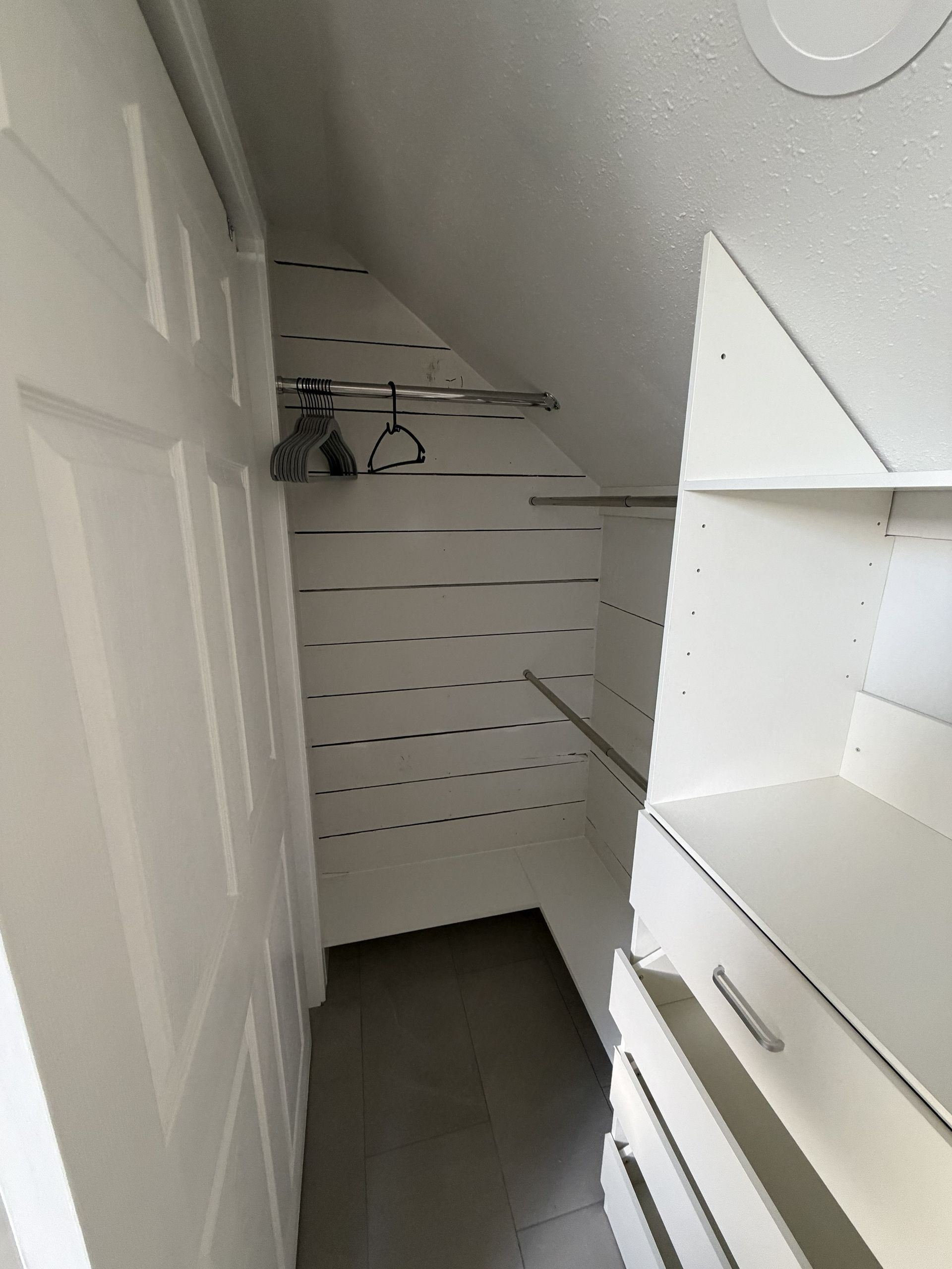 Narrow walk-in closet with white shelves, hanging rods, and dark flooring