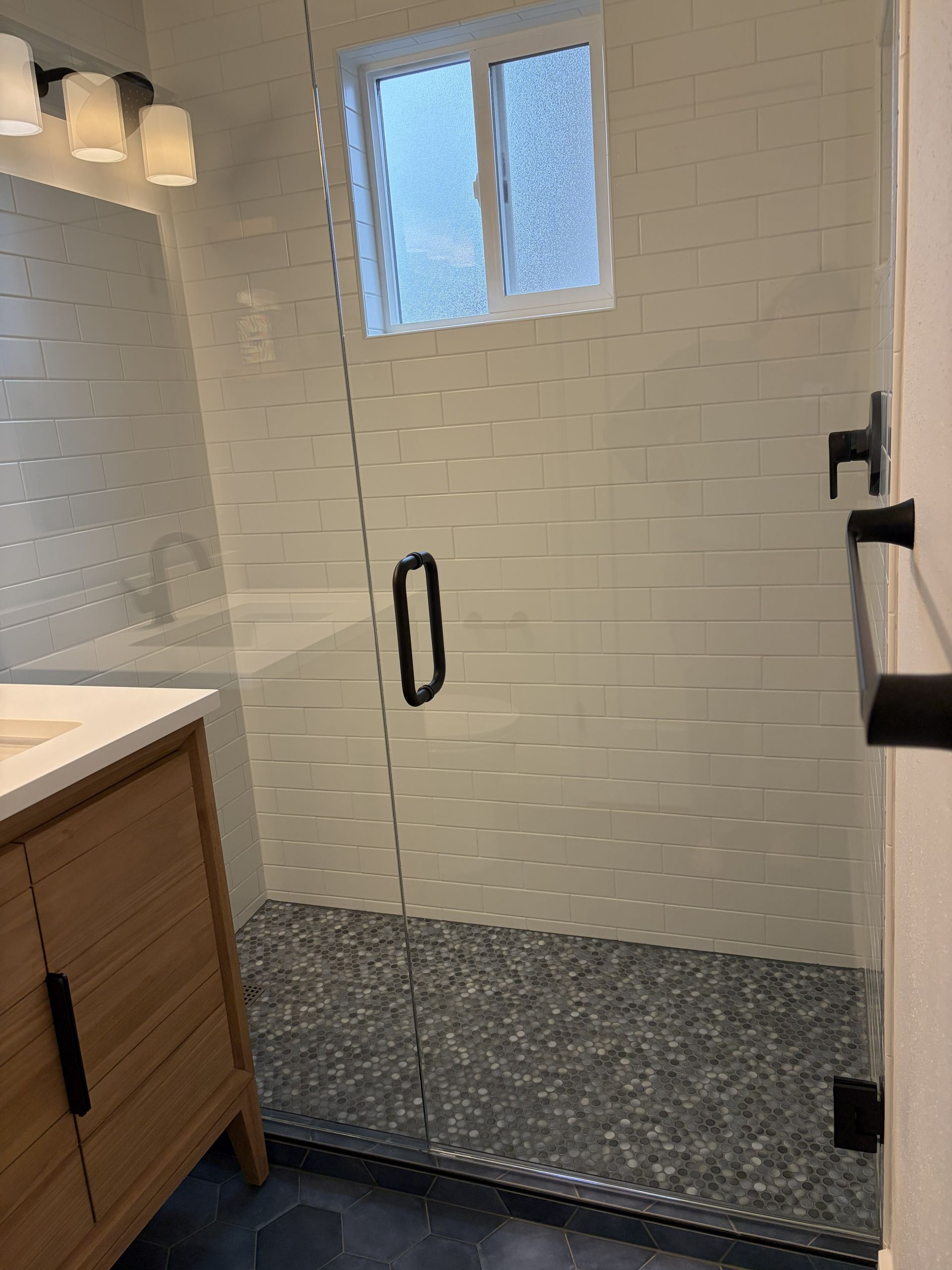 Modern bathroom shower with white subway tile, glass door, and small frosted window