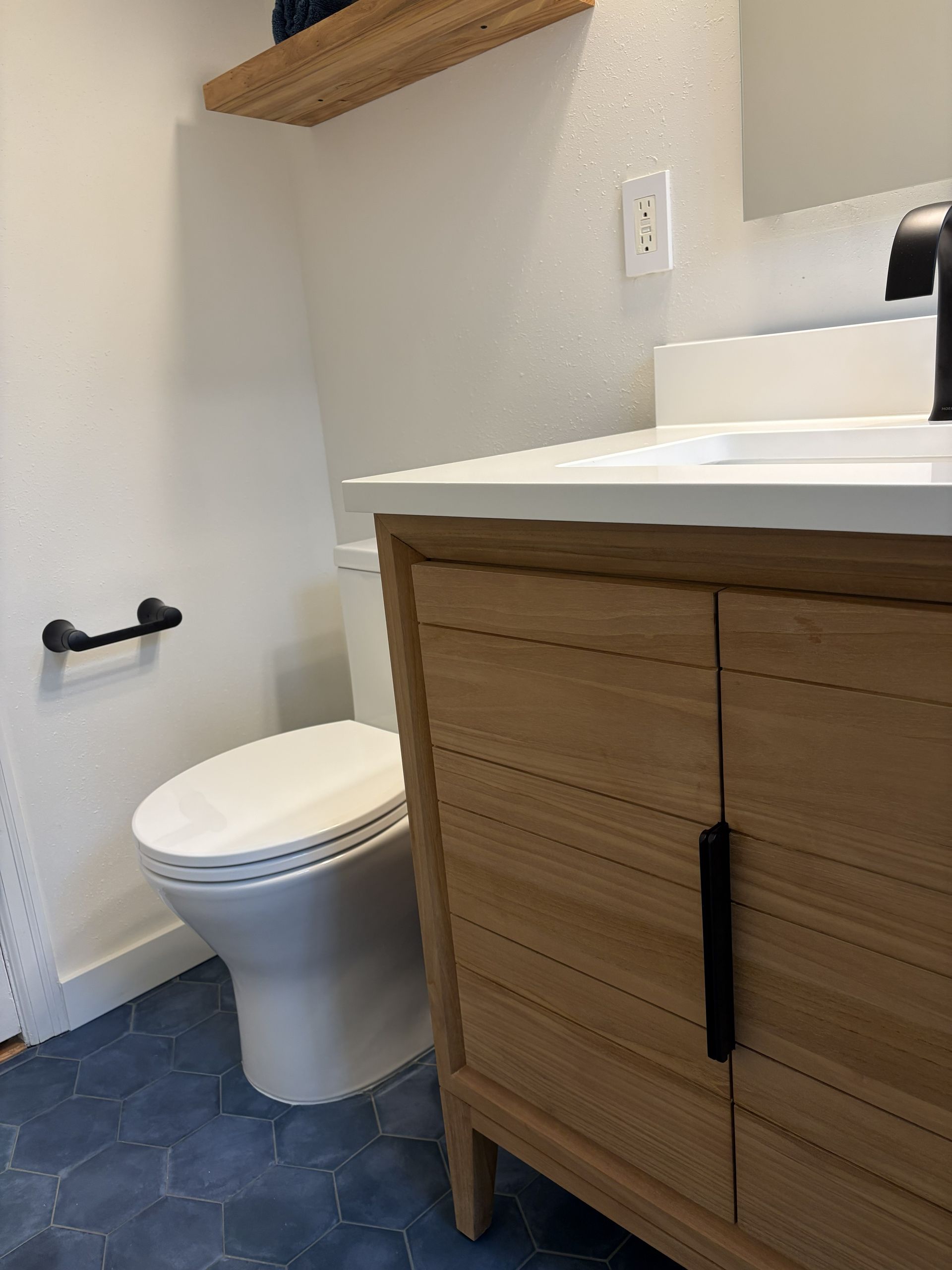 Small bathroom with white toilet, wood vanity, and blue tiled floor.