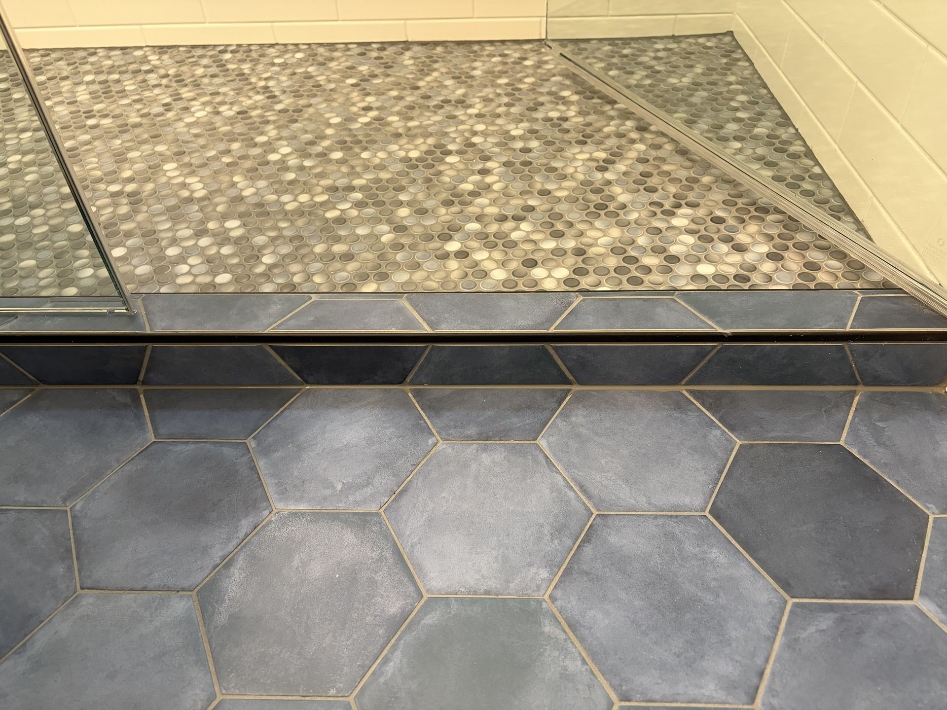 Hexagonal gray floor tiles meet a raised mosaic-tile threshold beside a beige wall.