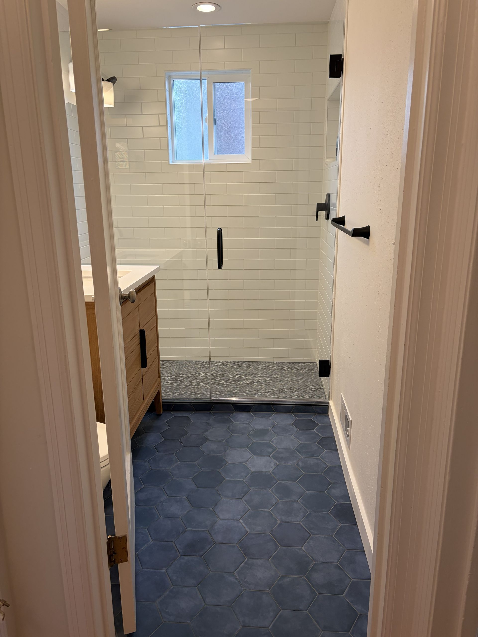 Narrow bathroom with blue floor tiles, white subway-tile shower, small window, and sink cabinet.
