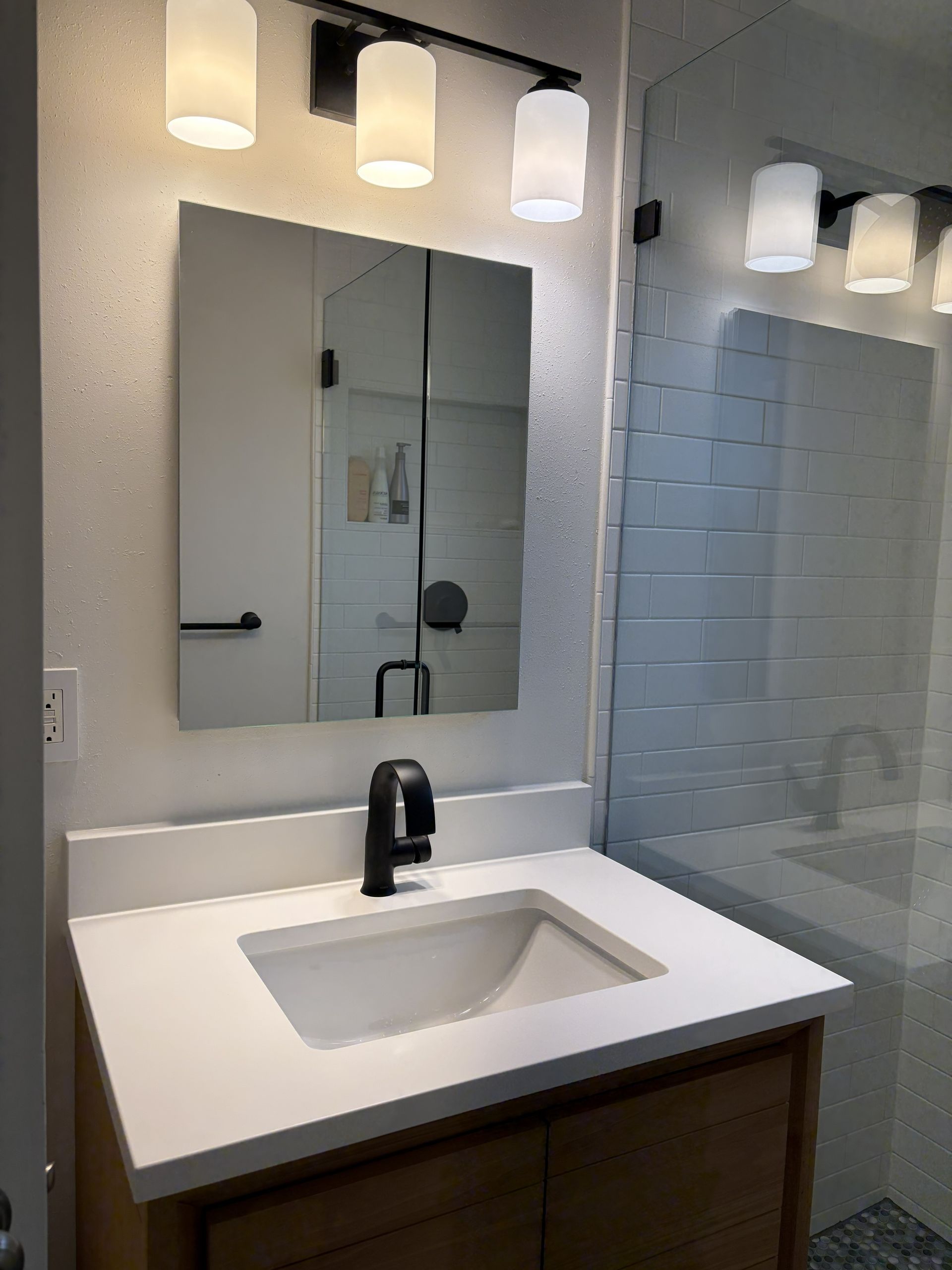 Modern bathroom vanity with white sink, black faucet, mirror, and three lights above.