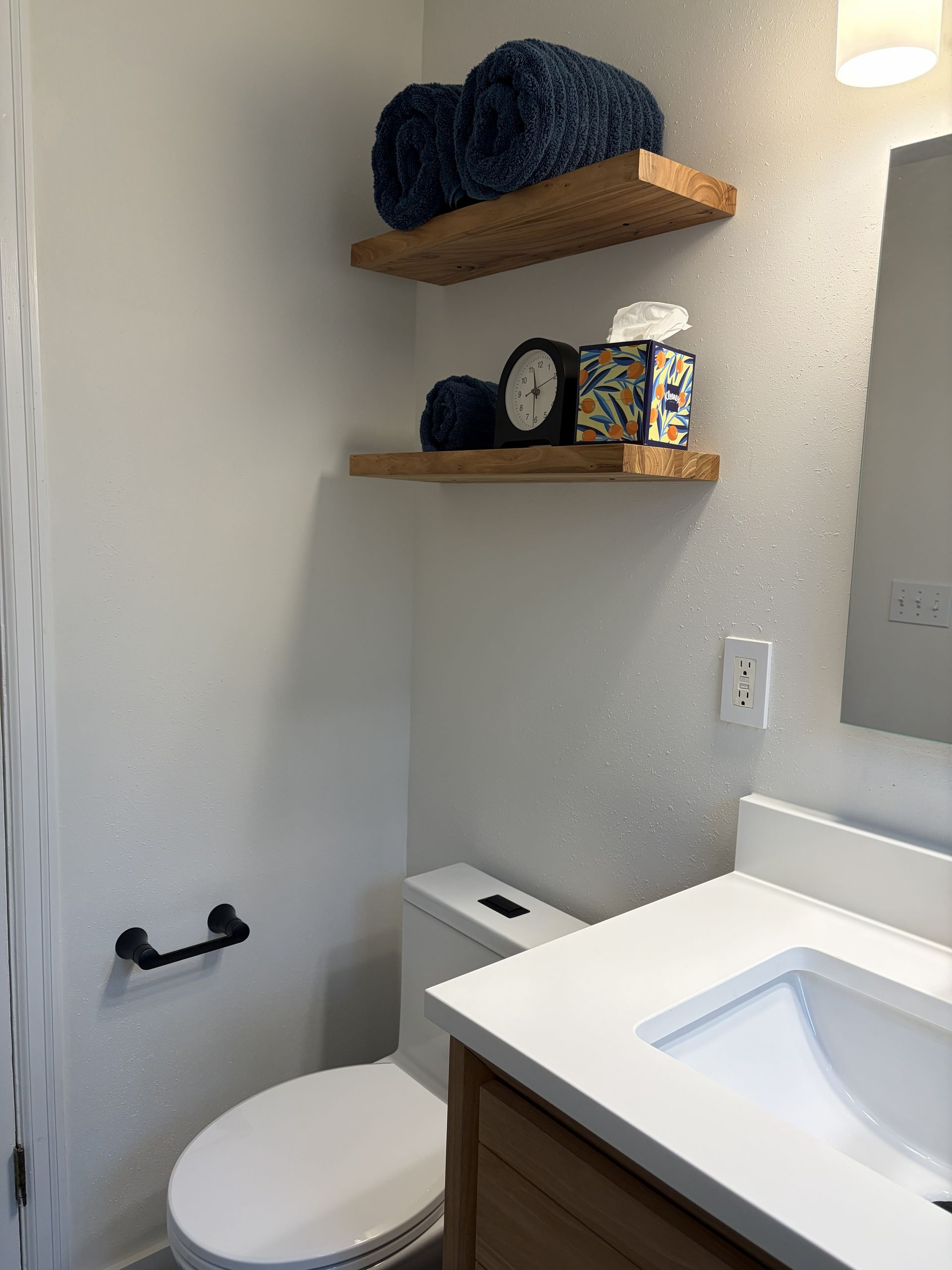 Small bathroom with toilet, sink, towel bar, and wooden shelves holding towels and toiletries.
