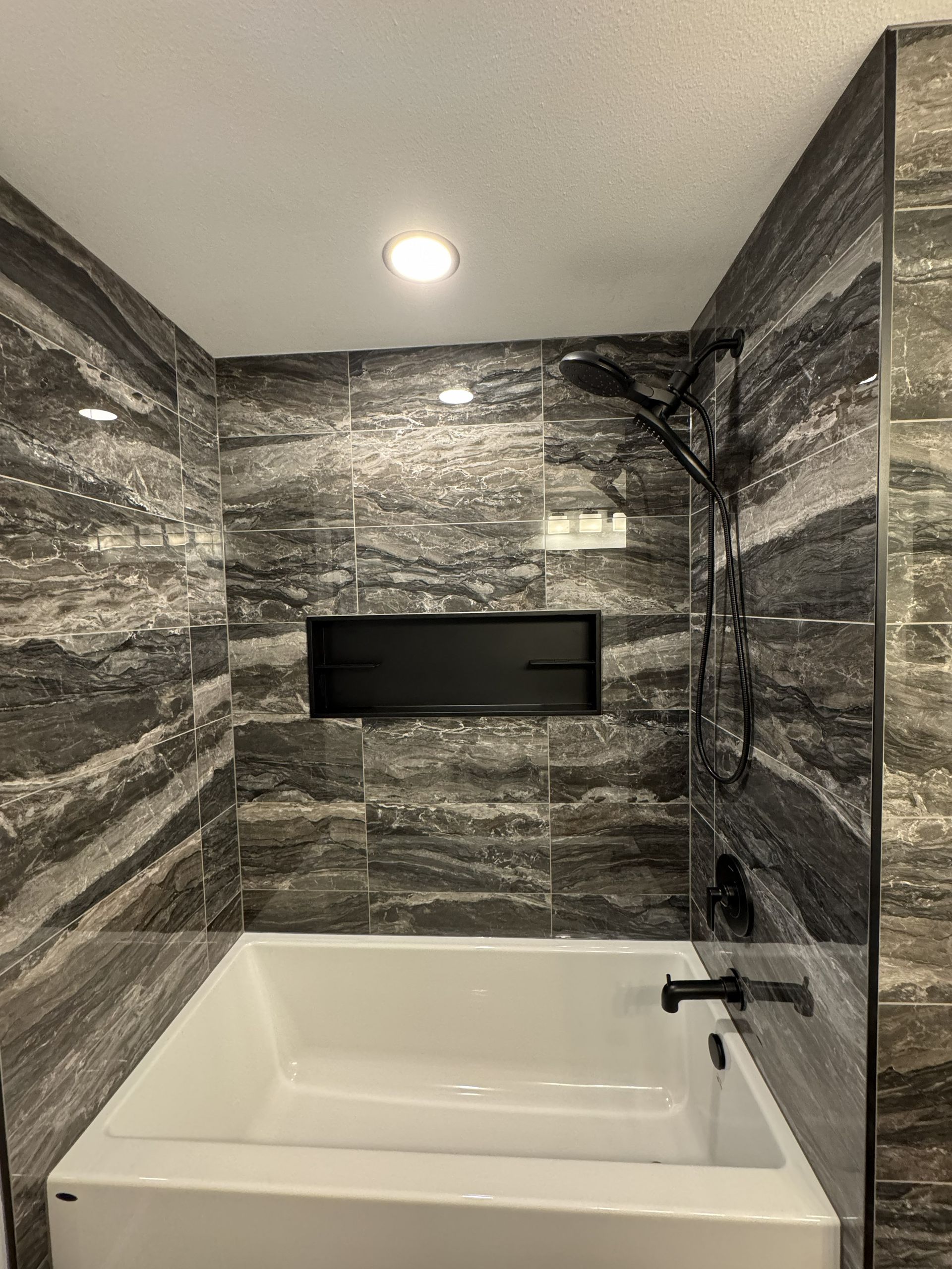 Modern bathroom with gray marble walls, a white bathtub, and a recessed wall niche above it.
