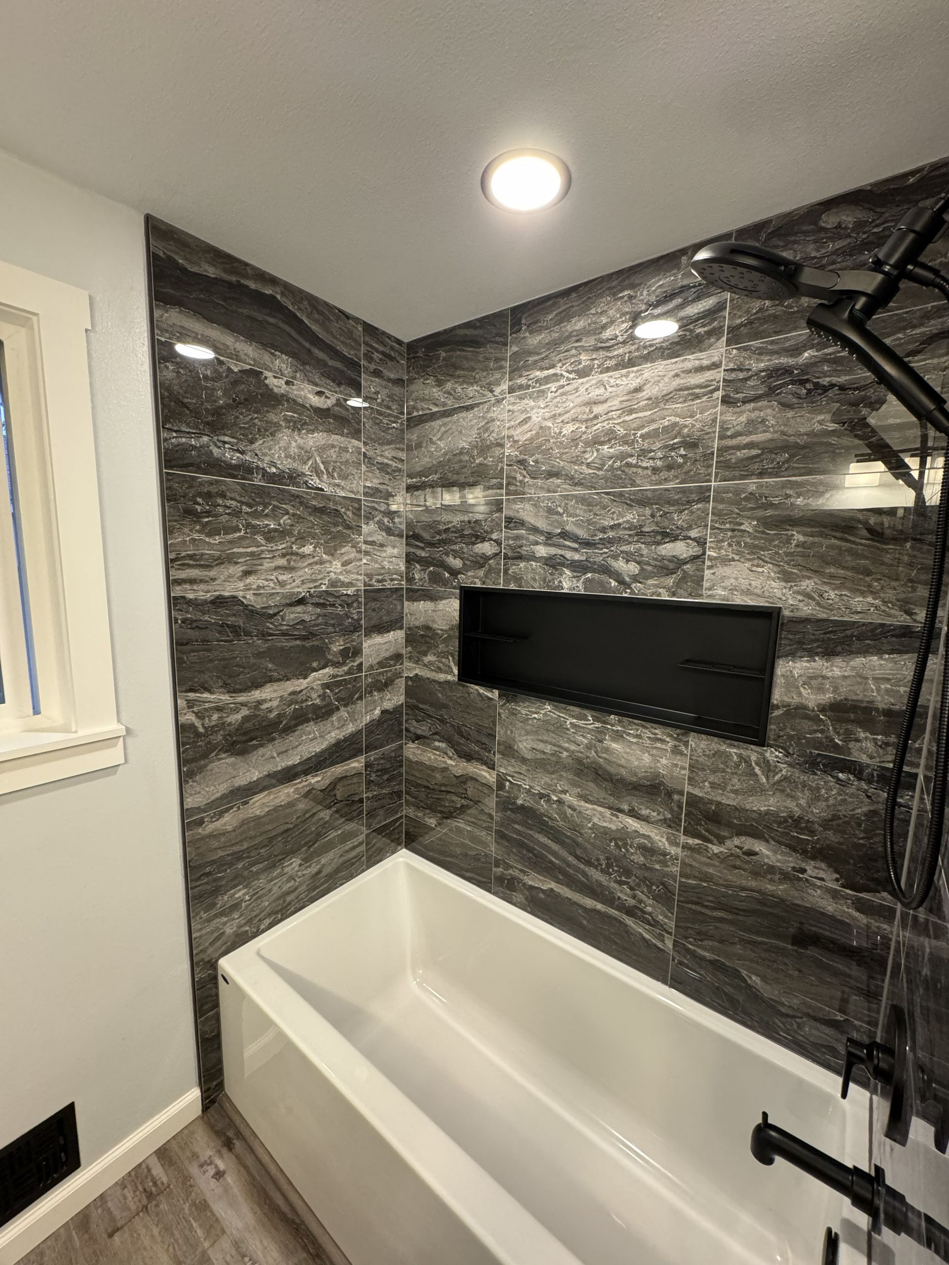 Modern bathroom with black marble tile shower, white tub, and black fixtures