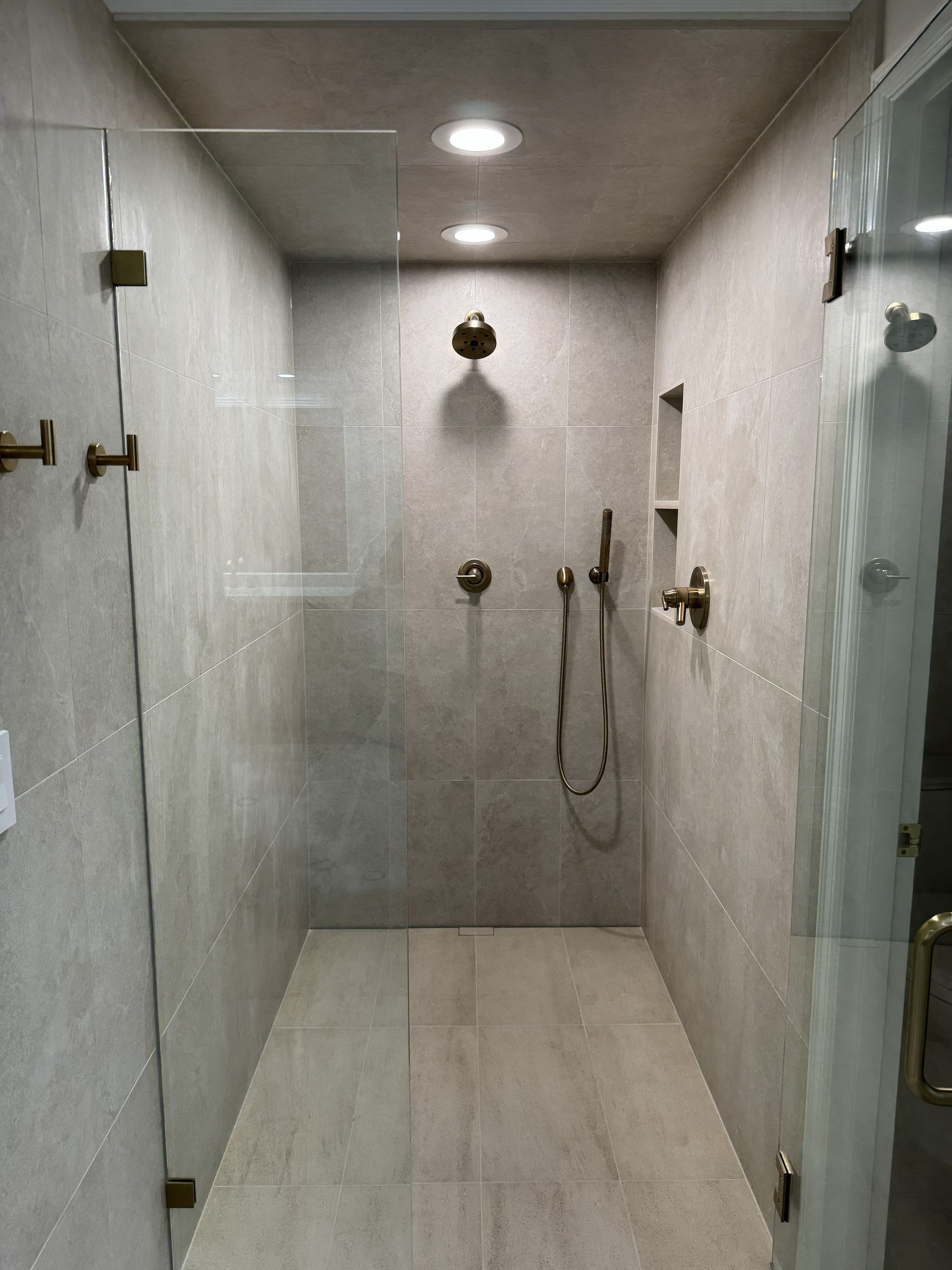 Empty tiled shower with multiple showerheads and handheld sprayer in a beige bathroom