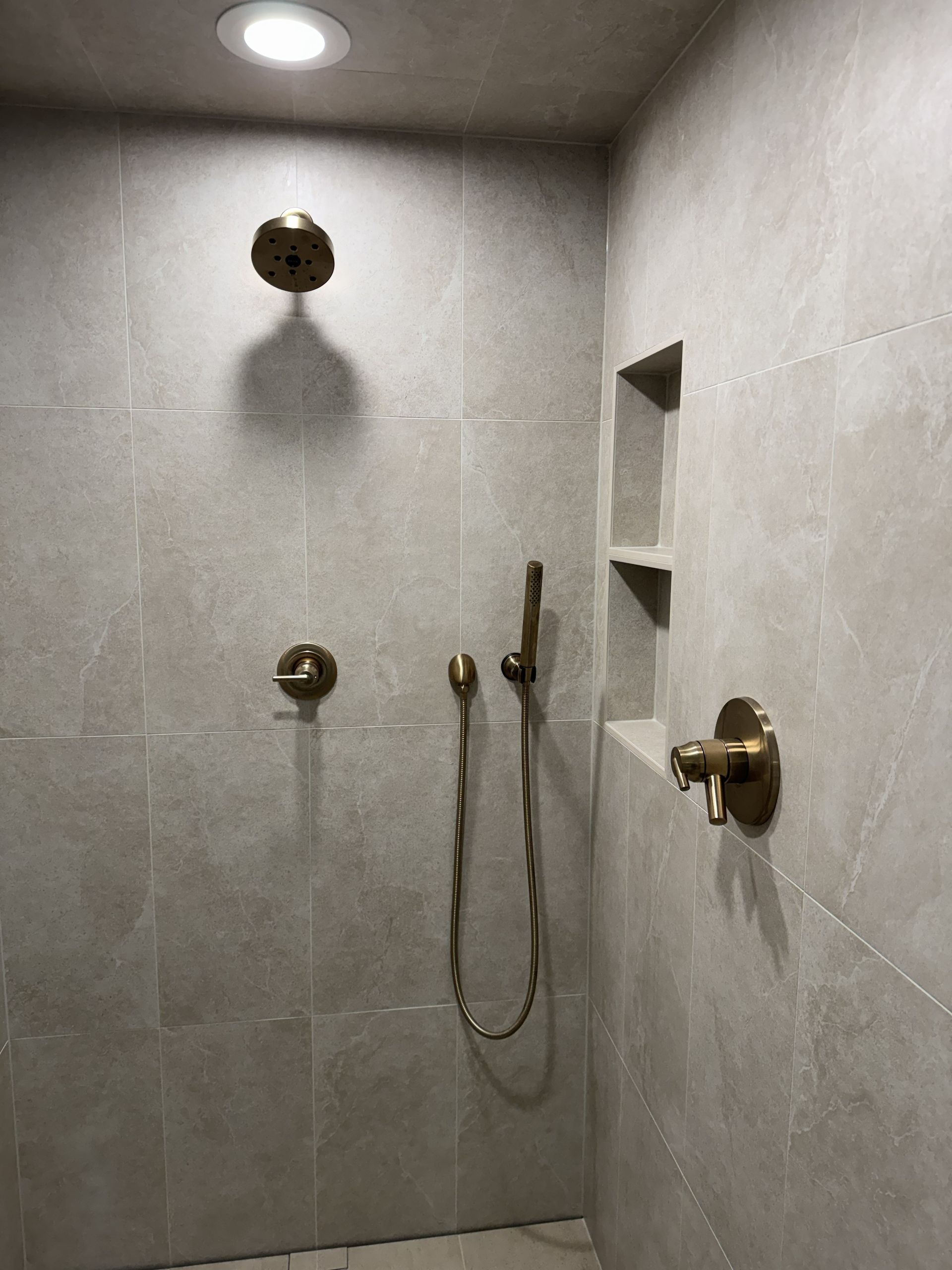 Empty gray-tiled shower with brass fixtures and a ceiling light
