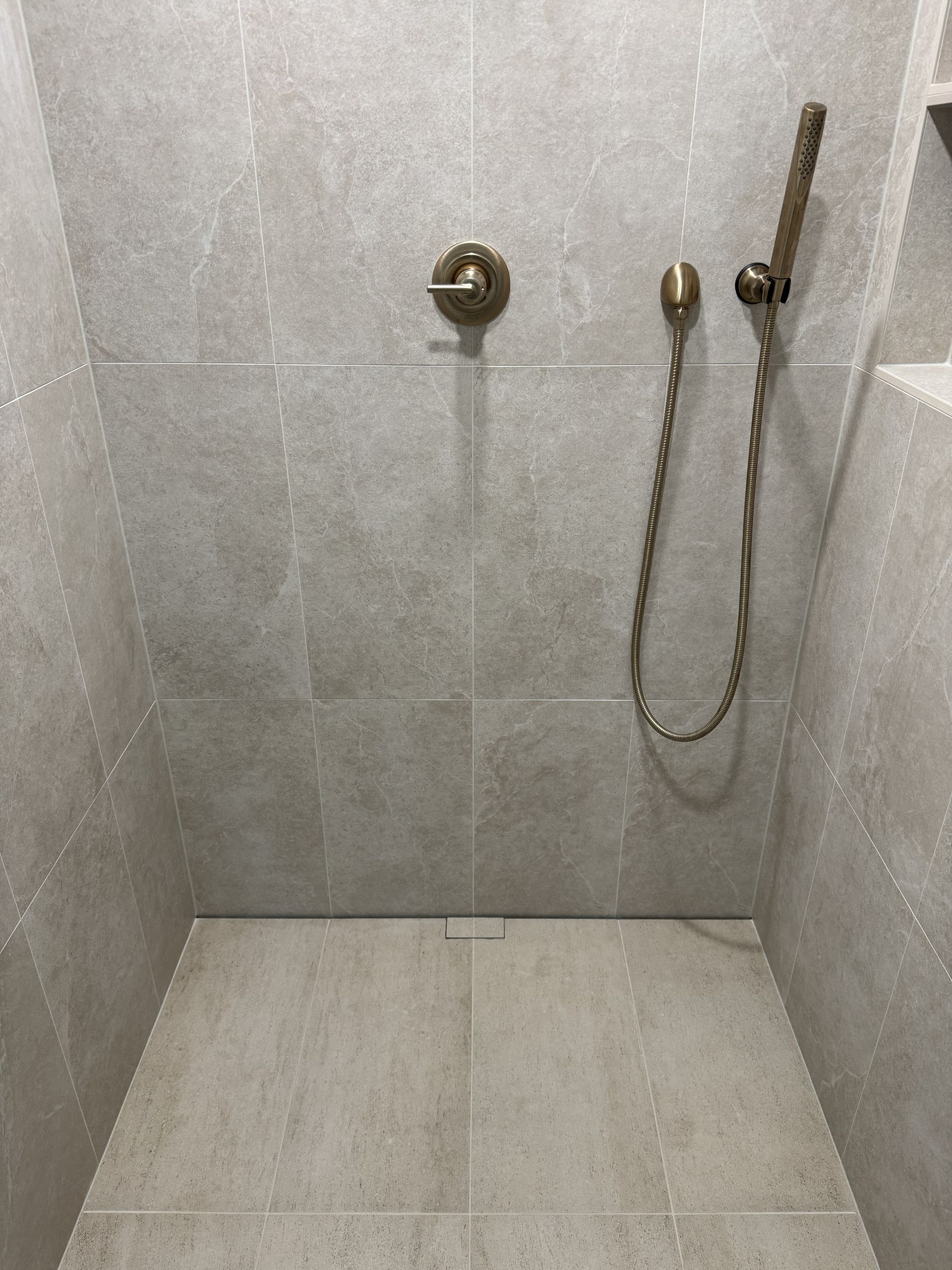 Empty tiled shower with wall-mounted faucets and a handheld showerhead.