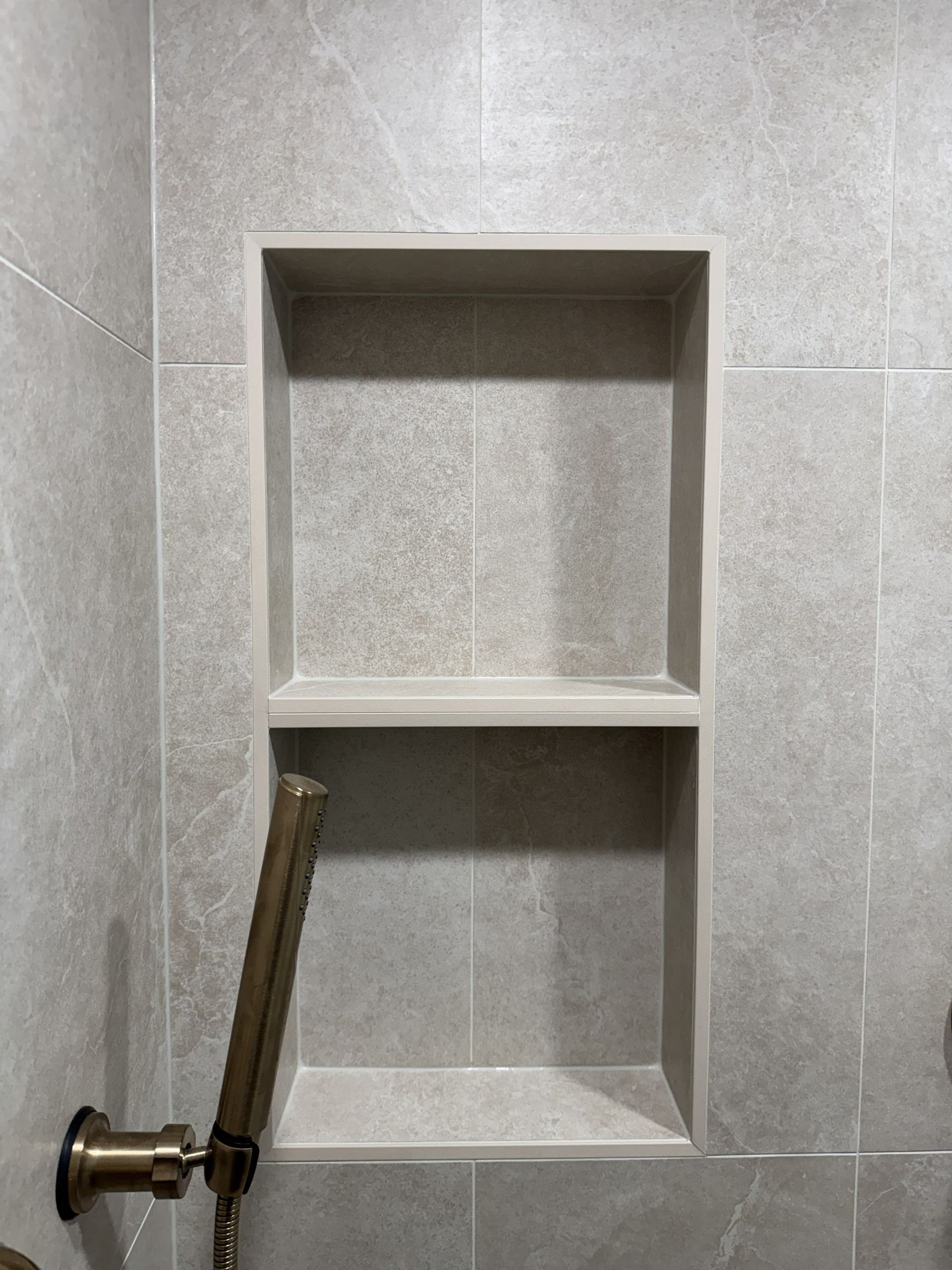 Tiled shower wall with recessed shelf niches and a shower valve handle on the left