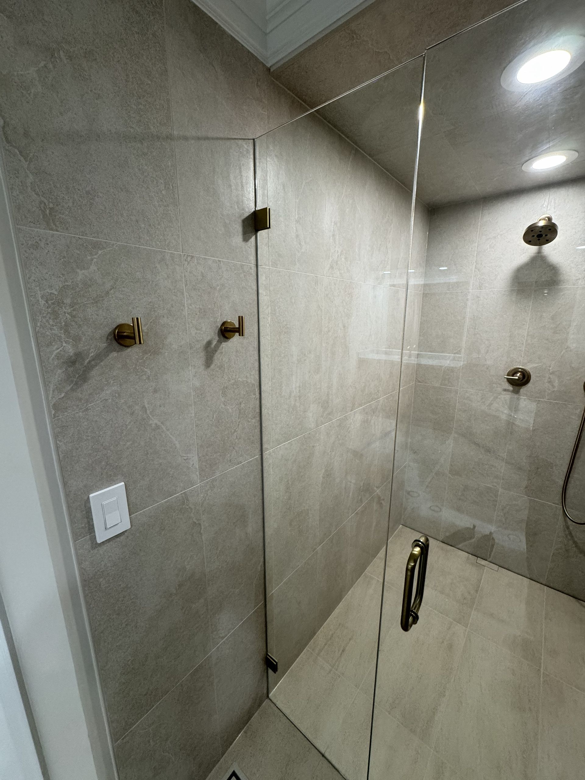 Empty tiled shower stall with glass door and chrome fixtures