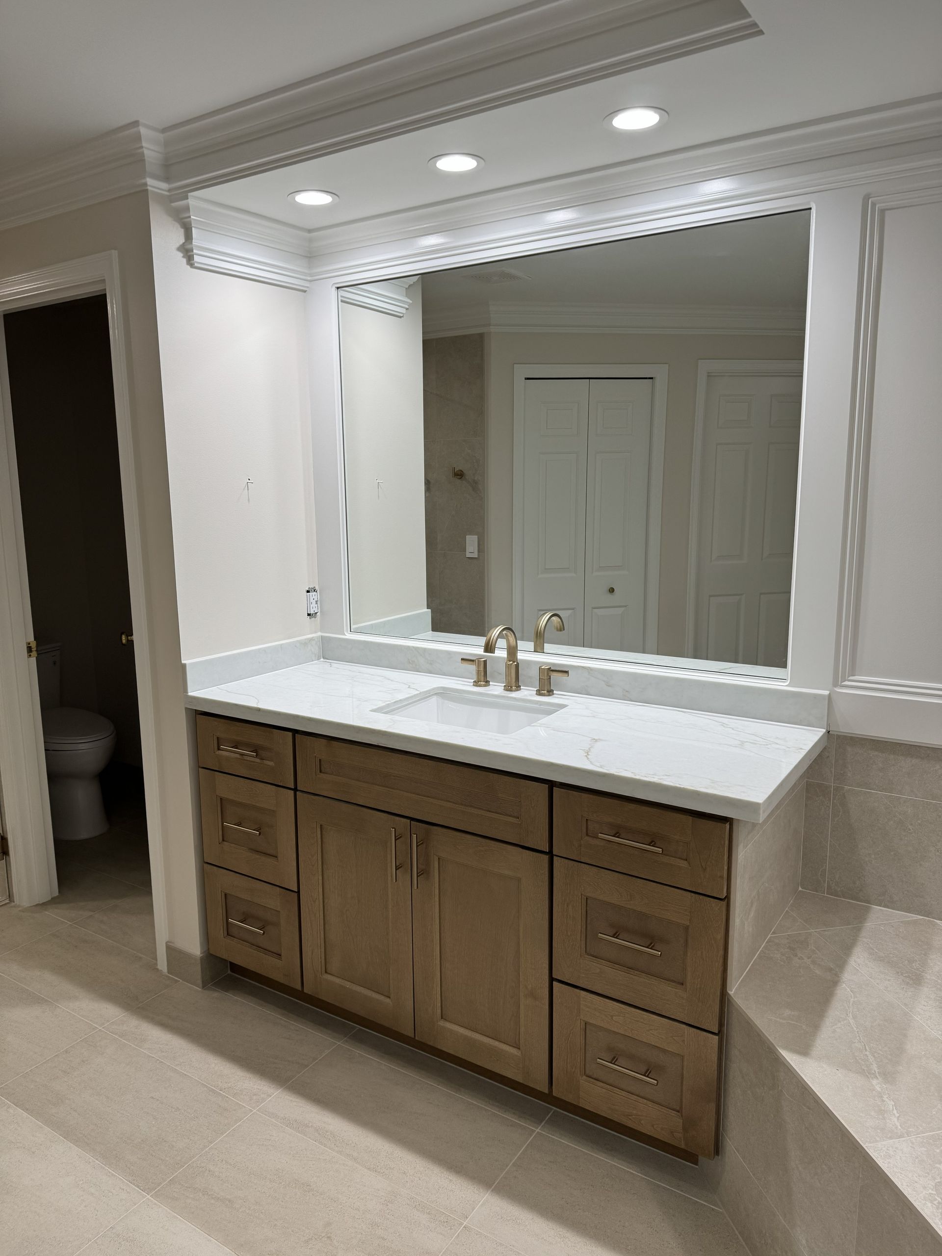 Elegant bathroom vanity with large illuminated mirror, white countertop, and wood cabinets.