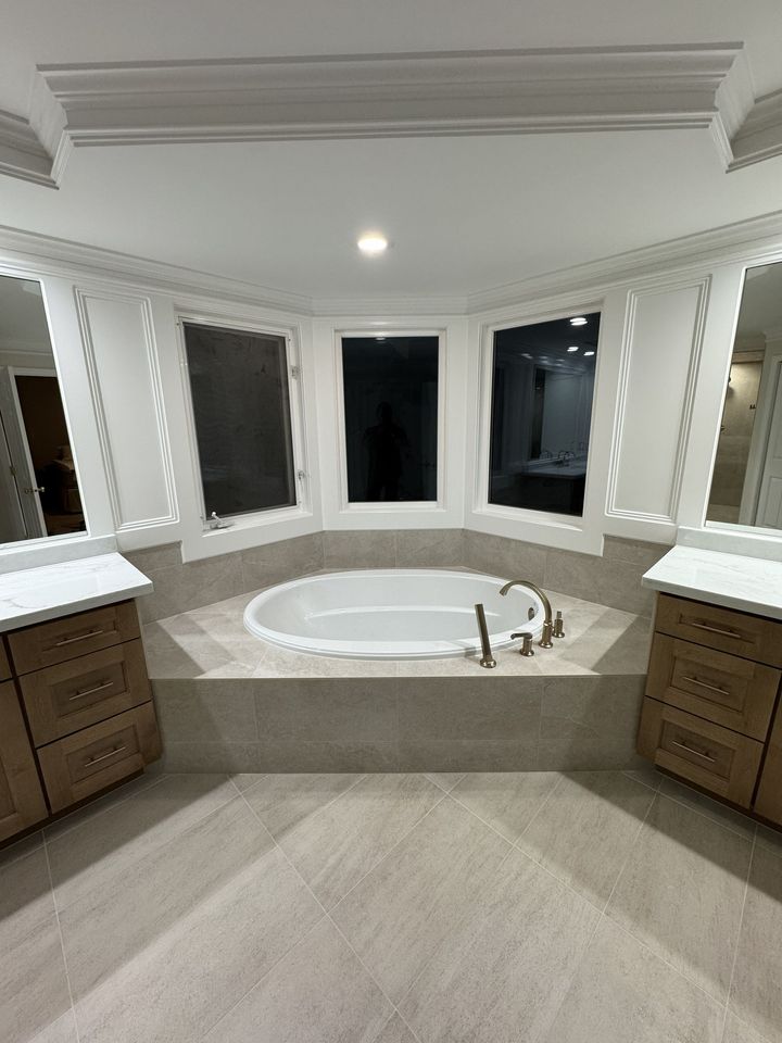 Modern bathroom with large soaking tub, twin vanities, and a bay of windows at night