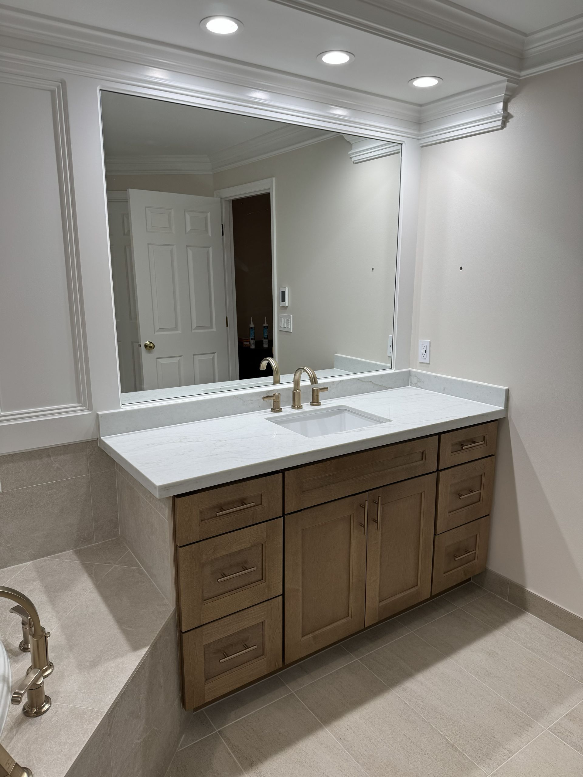 Bathroom vanity with large mirror, white countertop, and wooden cabinets under recessed ceiling lights