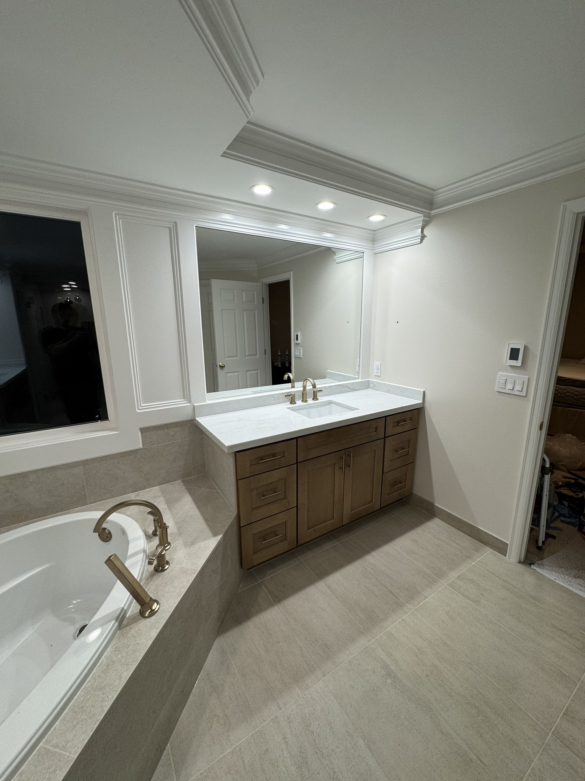 Modern bathroom with double vanity, large mirror, white countertops, and a bathtub in the foreground