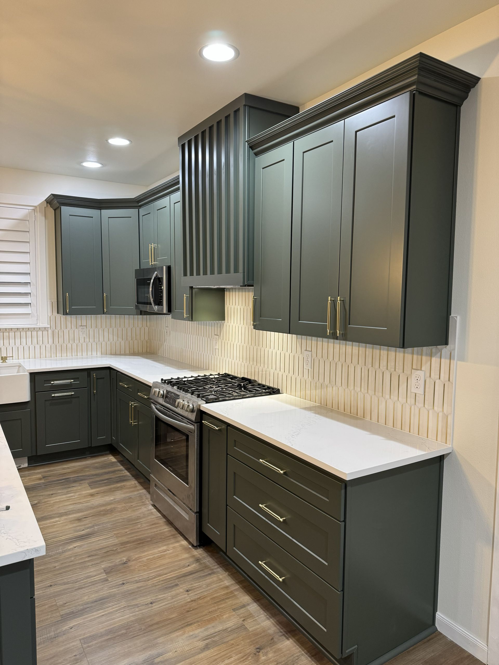 Modern kitchen with dark green cabinets, white countertops, stainless appliances, and wood-look flooring