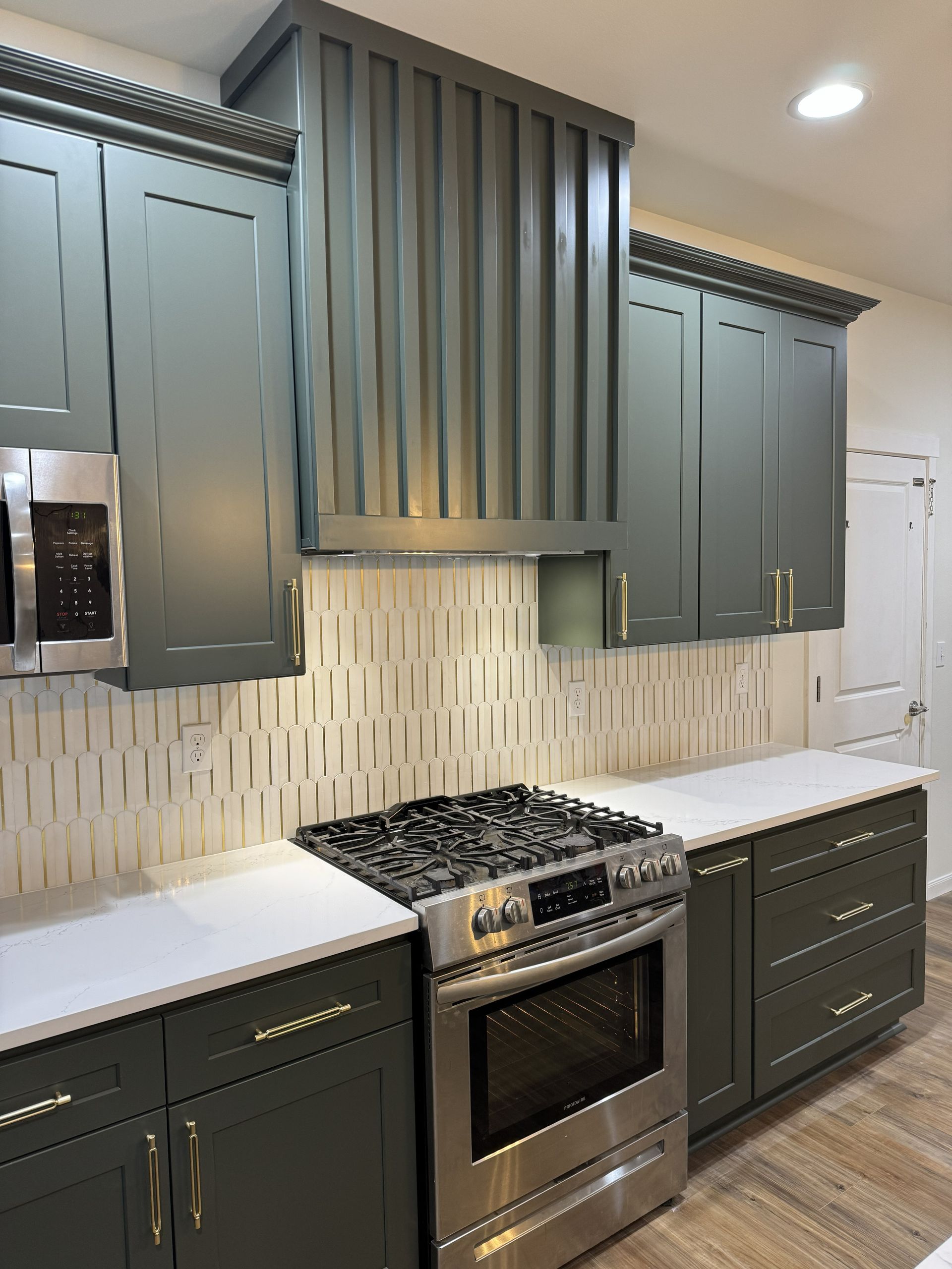 Modern kitchen with sage green cabinets, stainless steel stove, white countertops, and tiled backsplash.