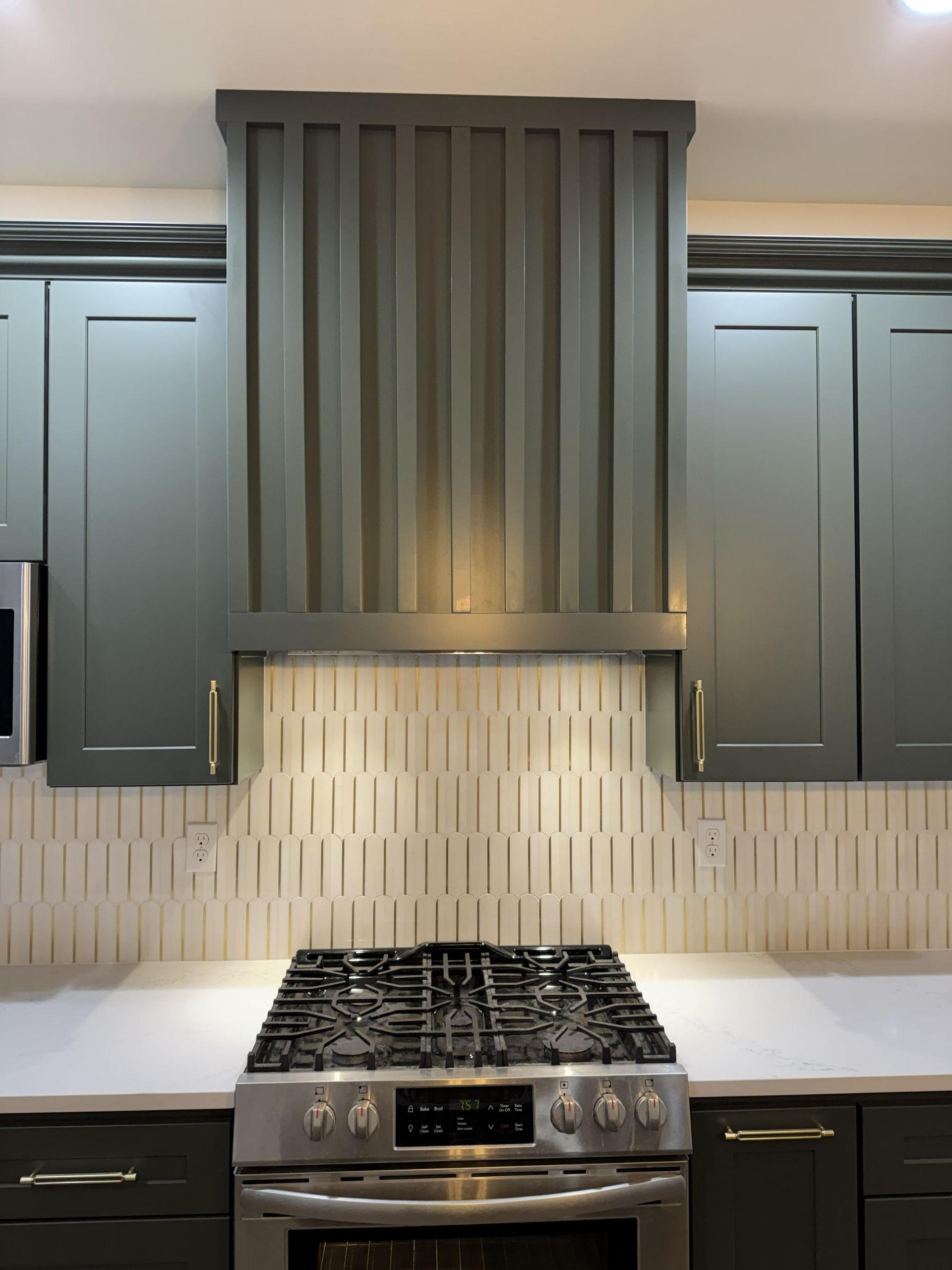Modern kitchen with dark cabinets, patterned tile backsplash, and stainless steel stove centered below a hood.