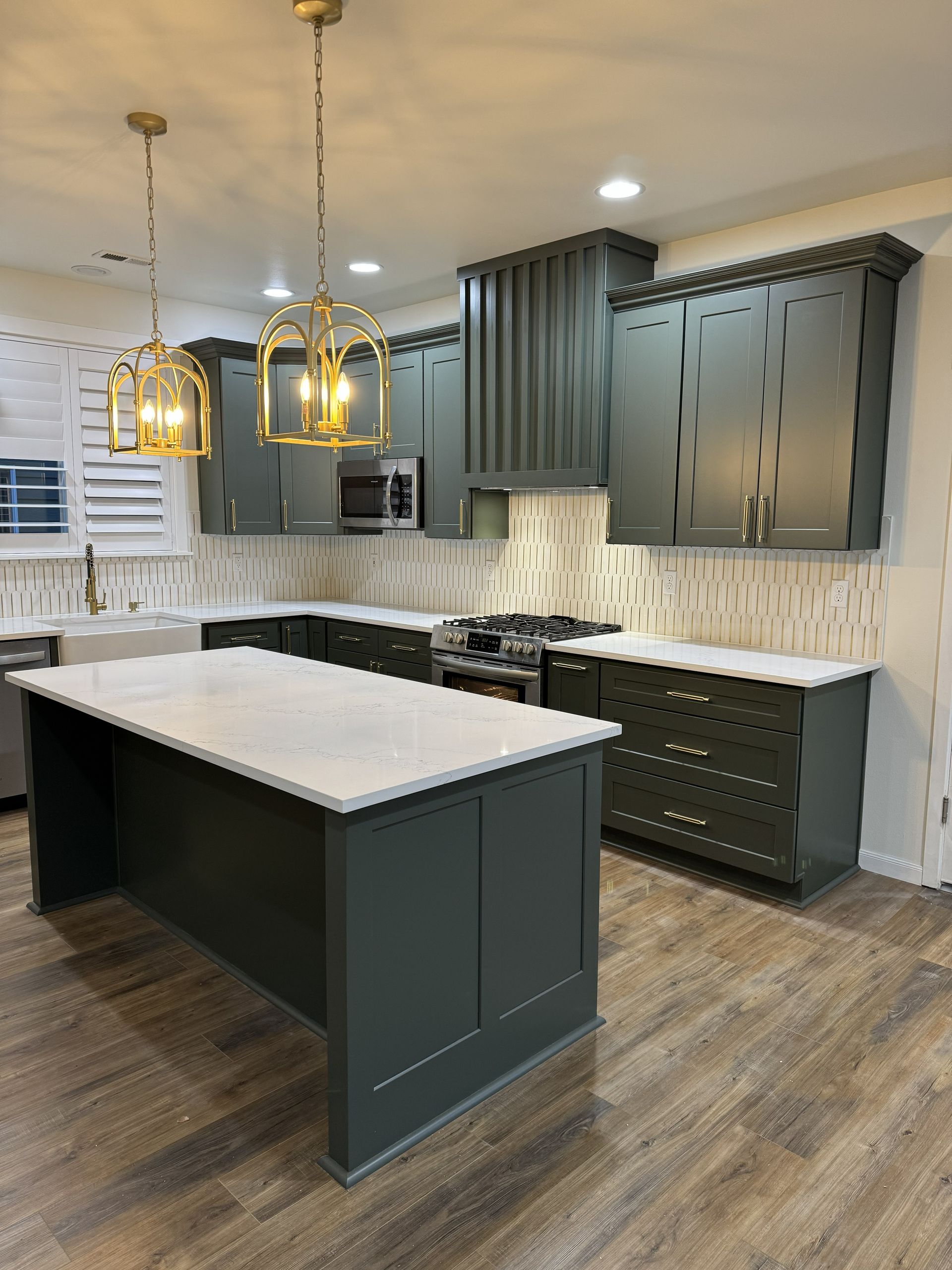 Modern kitchen with dark gray cabinets, white island countertop, and gold pendant lights