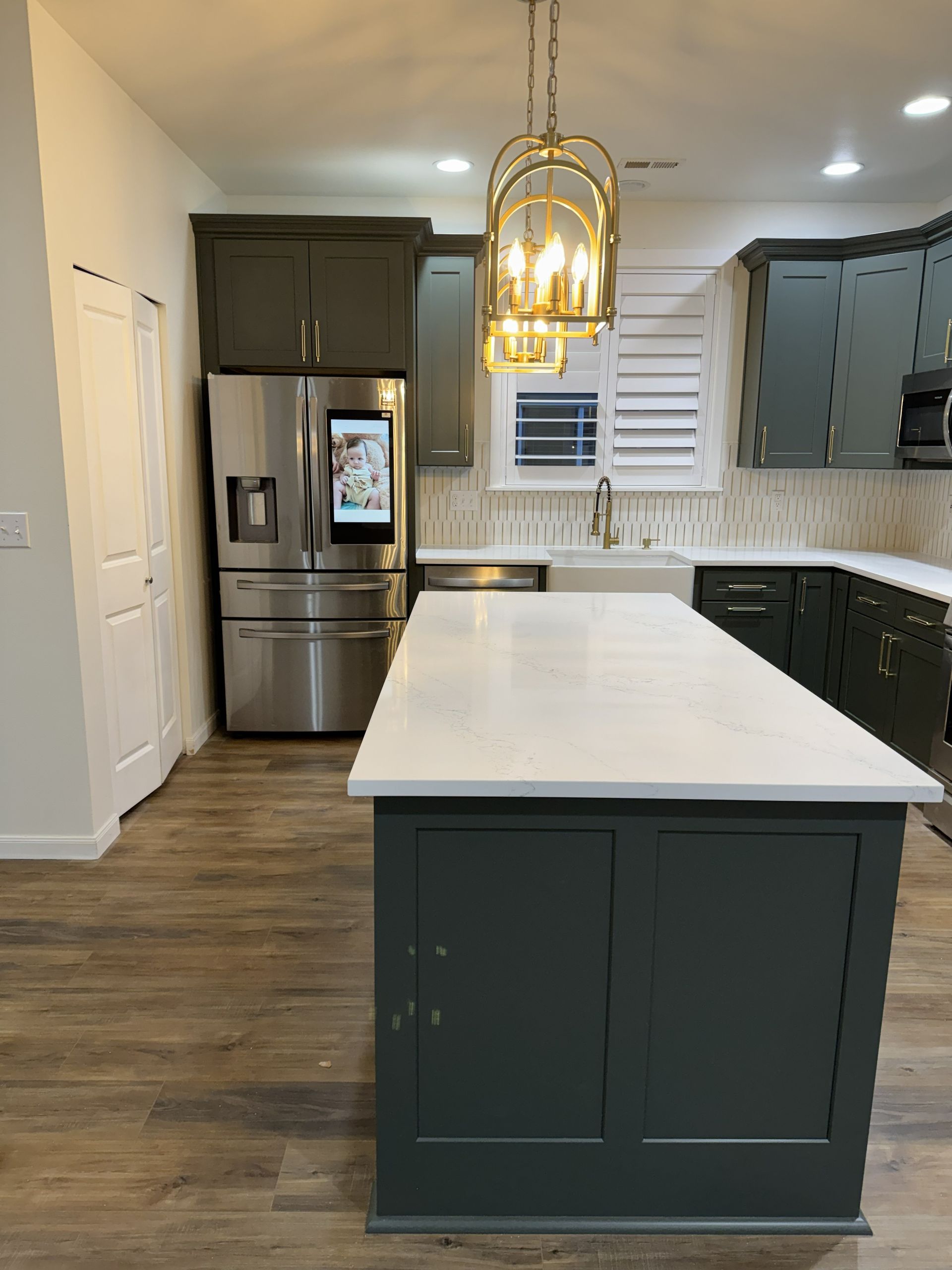 Modern kitchen with dark cabinets, white island, stainless fridge, and gold pendant lights