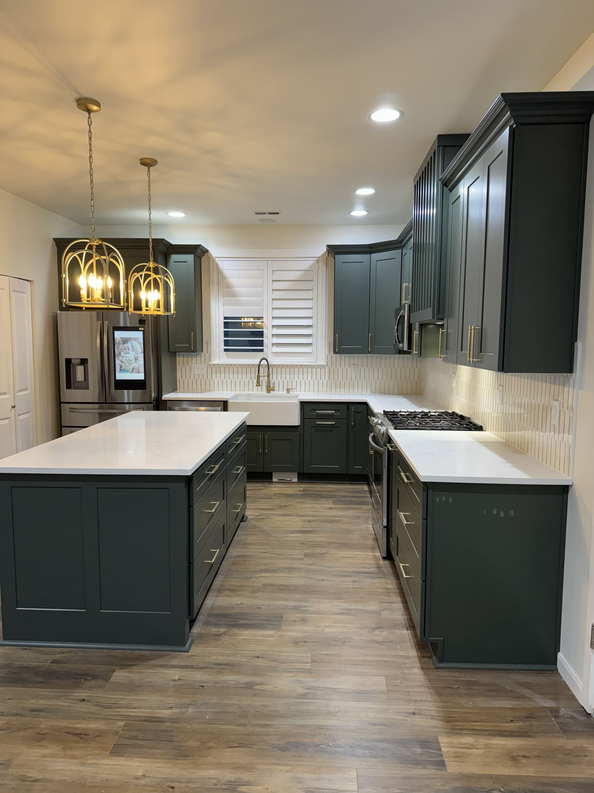 Modern kitchen with dark cabinets, white countertops, two islands, and wood-look flooring