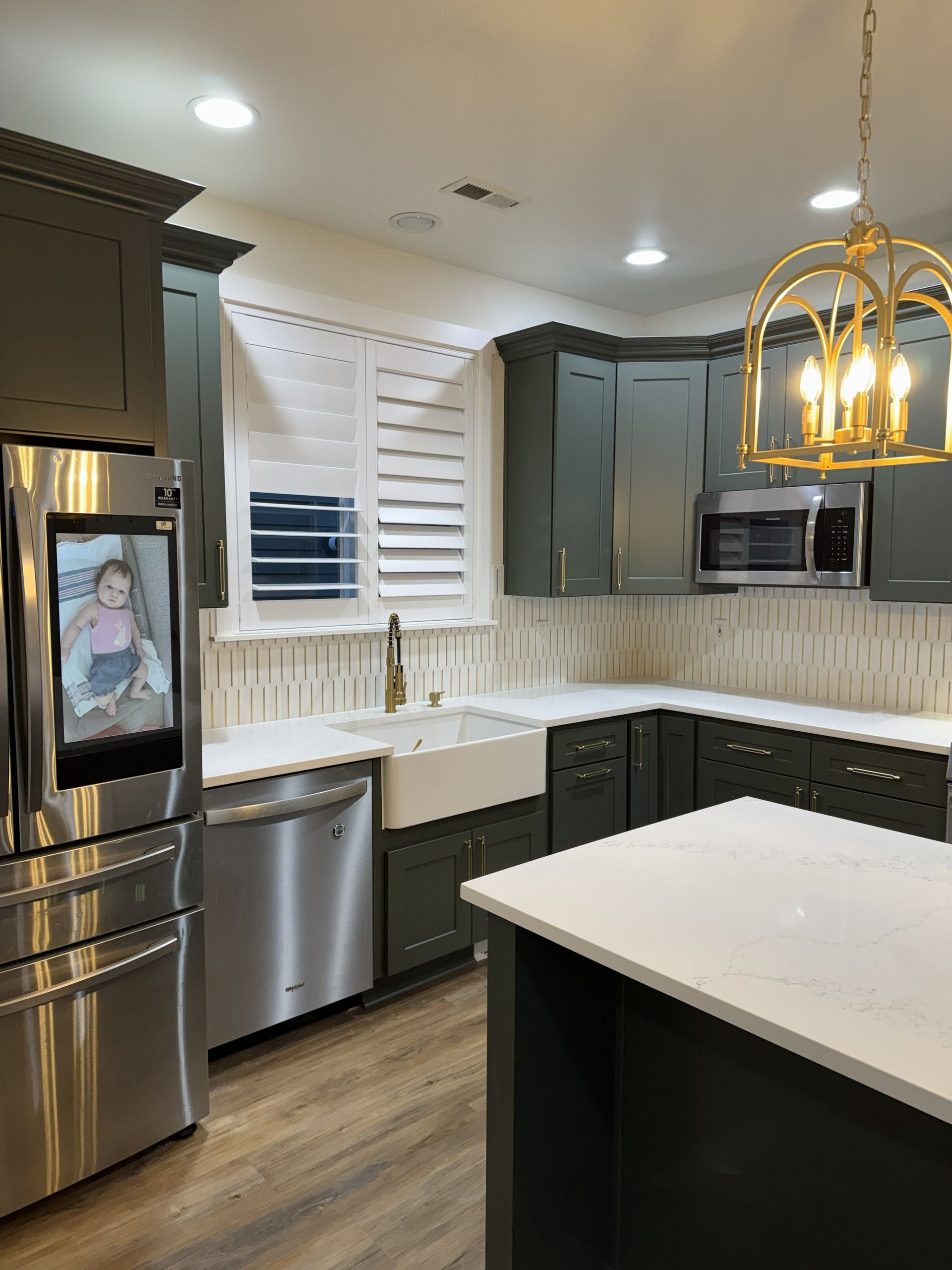 Modern kitchen with gray cabinets, stainless appliances, white countertops, and a large island.
