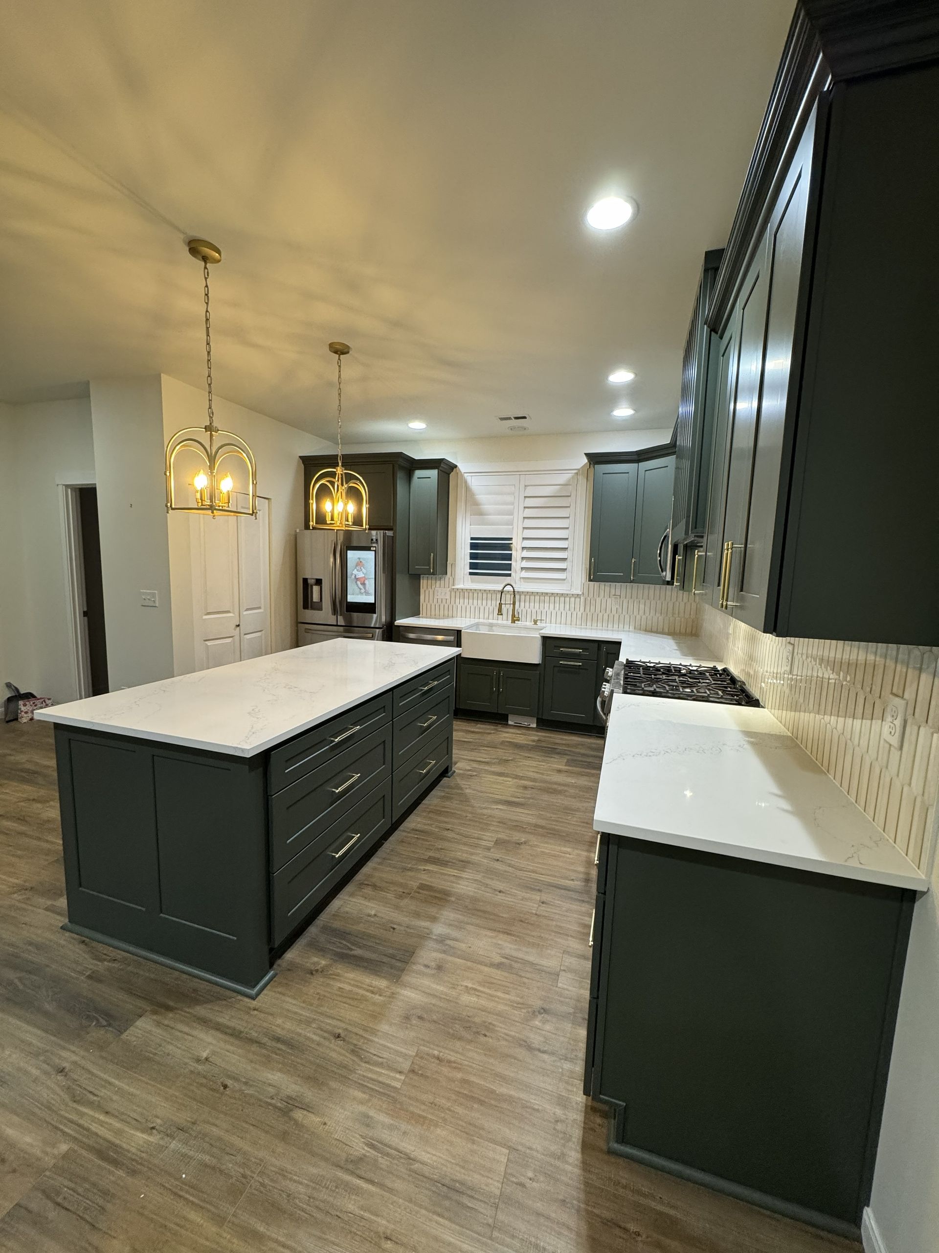Modern kitchen with dark island cabinets, white countertops, wood floors, and pendant lighting.