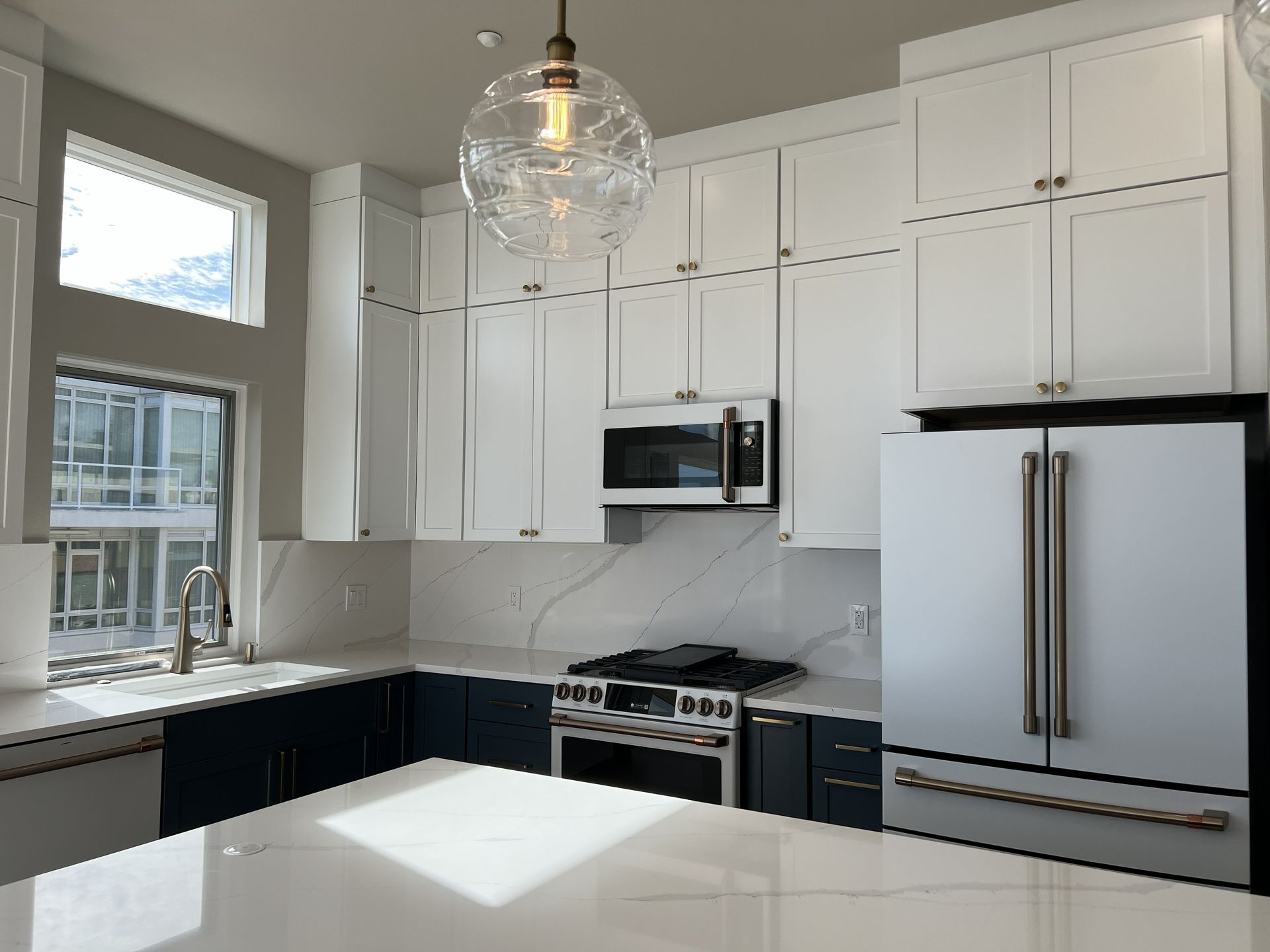 Bright white kitchen with black countertops, stainless steel appliances, and a large window above the sink.
