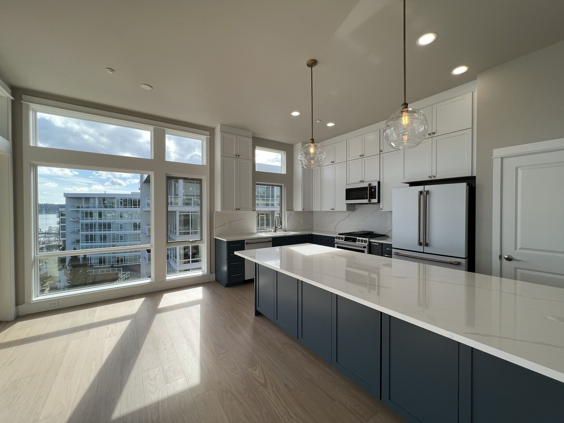 Bright modern kitchen with white island, navy cabinets, and large sunlit windows