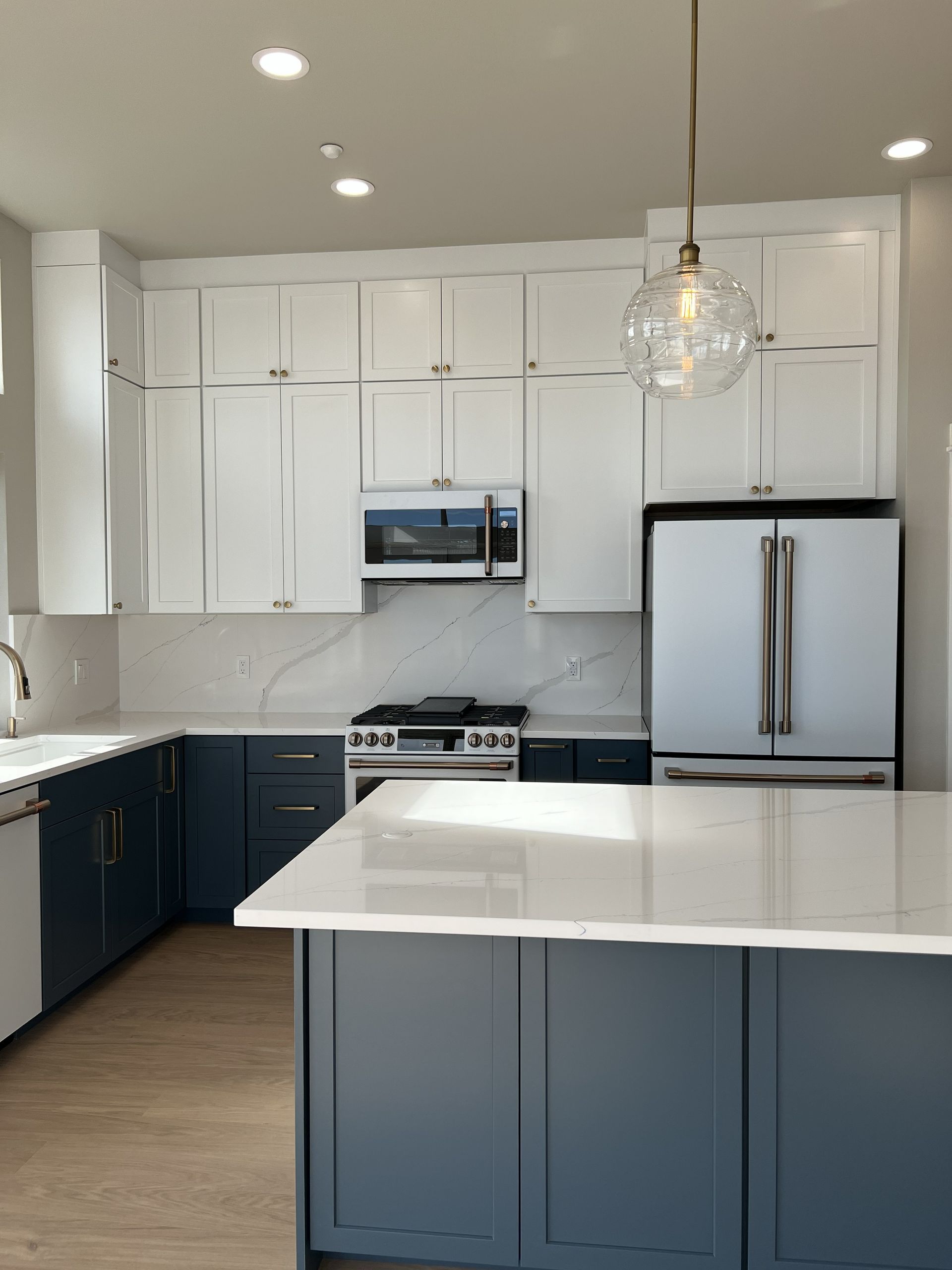 Modern kitchen with white upper cabinets, navy lower cabinets, stainless appliances, and a marble island