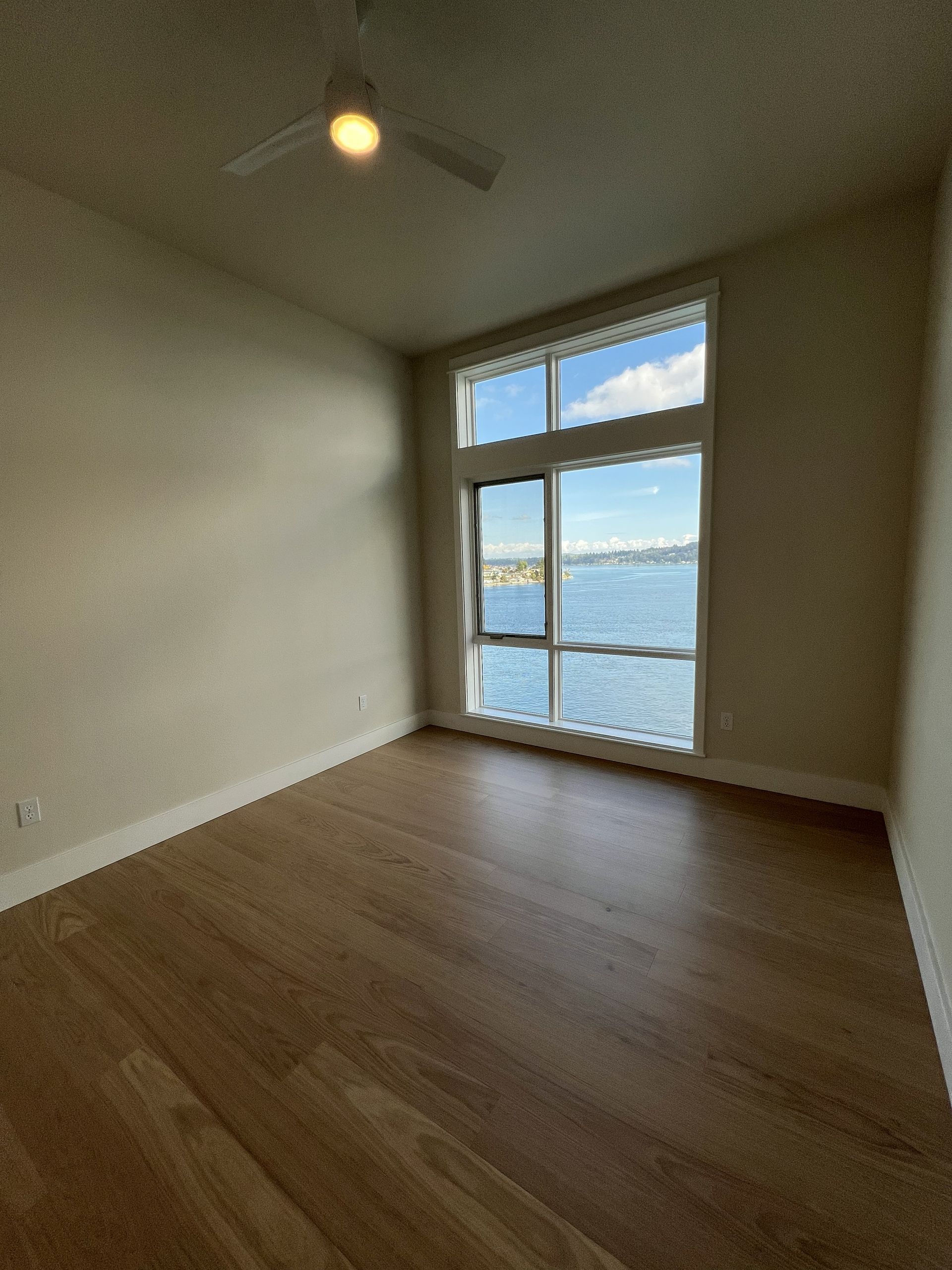 Empty unfurnished room with wood floor, large window, and view of water and sky