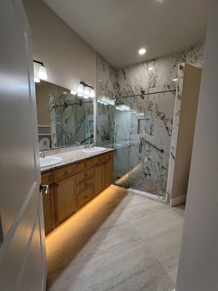 Modern bathroom with double vanity, wall mirrors, and marble shower enclosure with warm under-cabinet lighting