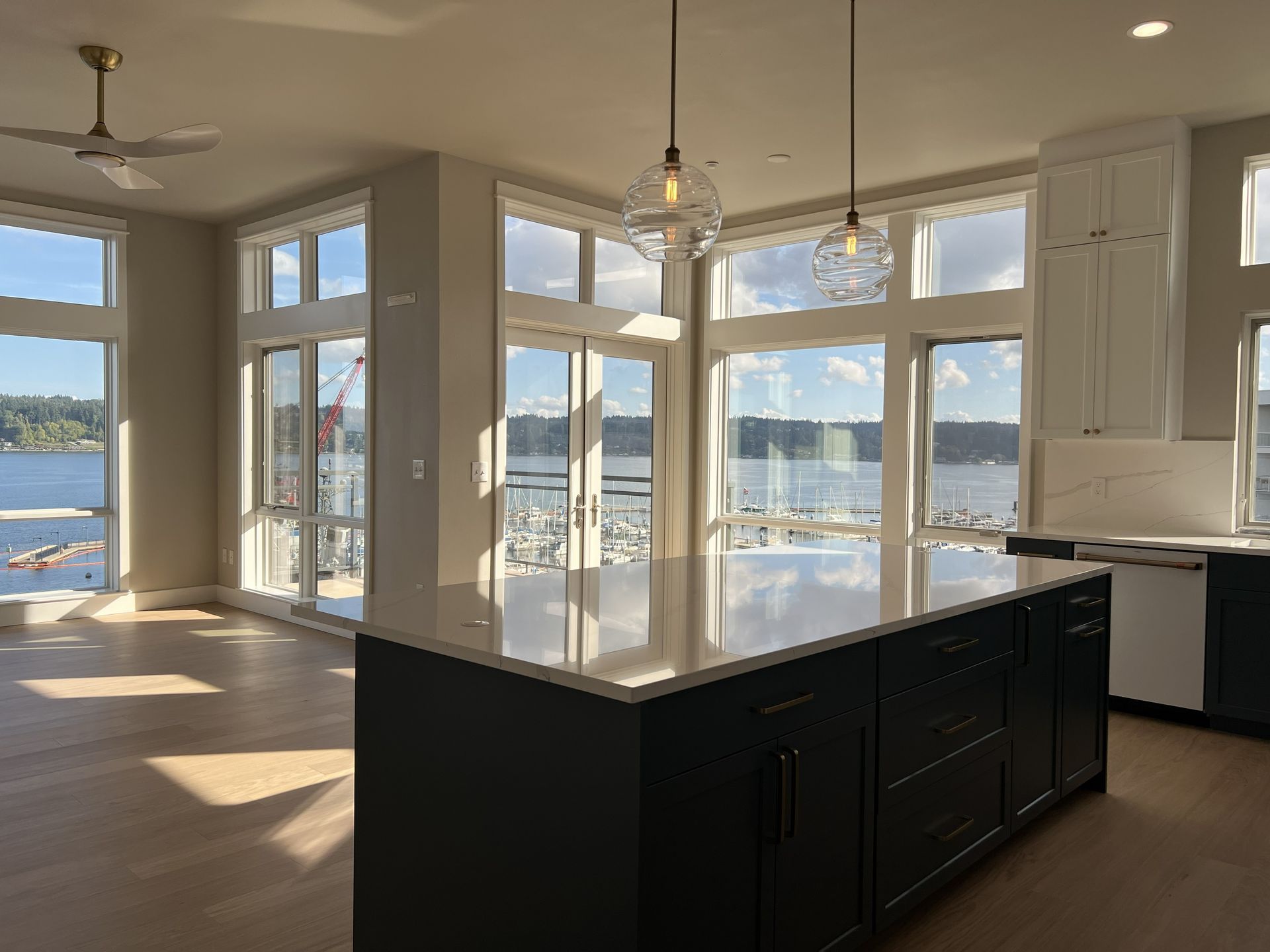 Bright open kitchen with a dark island, white cabinets, and large windows overlooking water and distant mountains