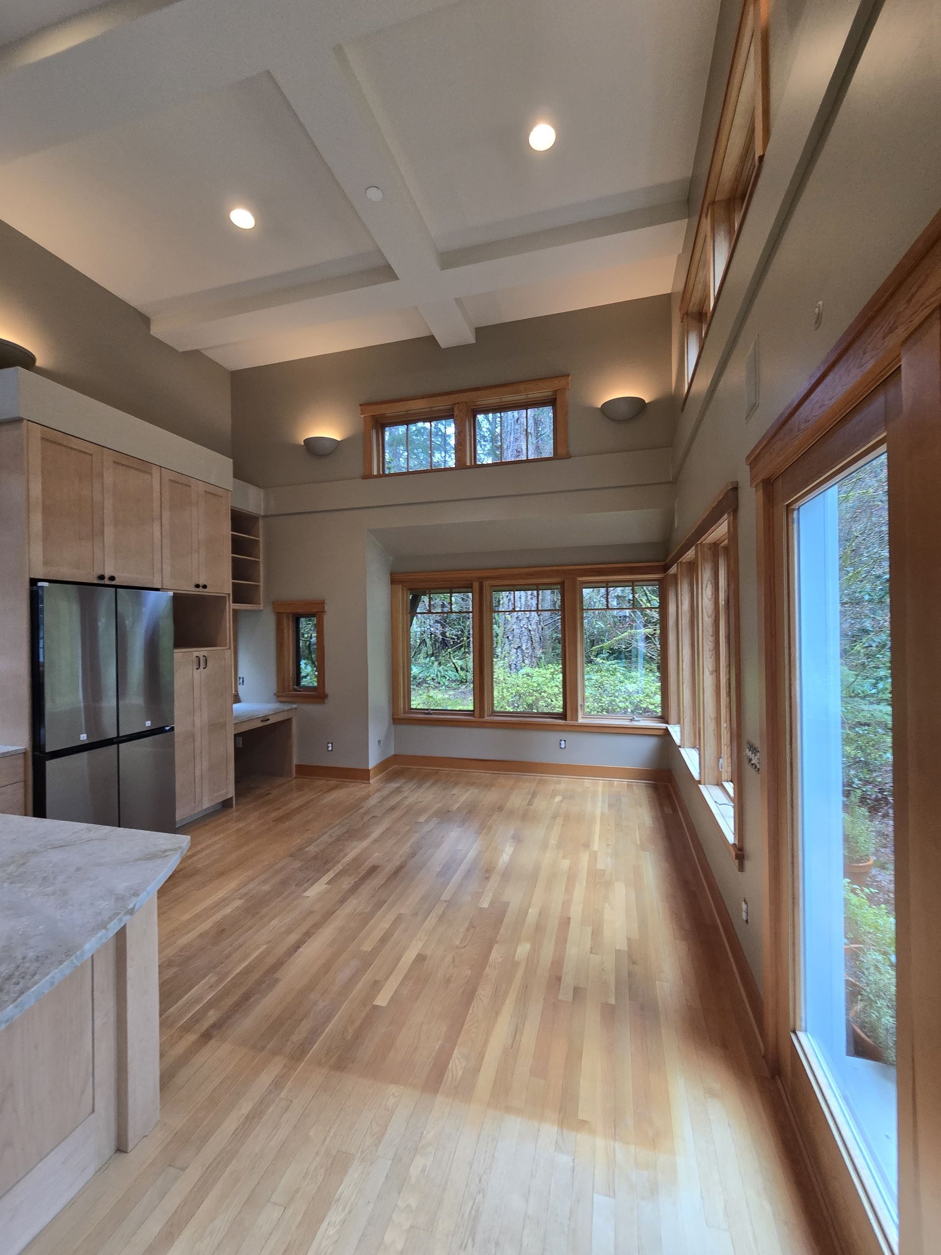 Spacious modern living room with wood floors, high ceilings, large windows, and a stainless steel kitchen on the left