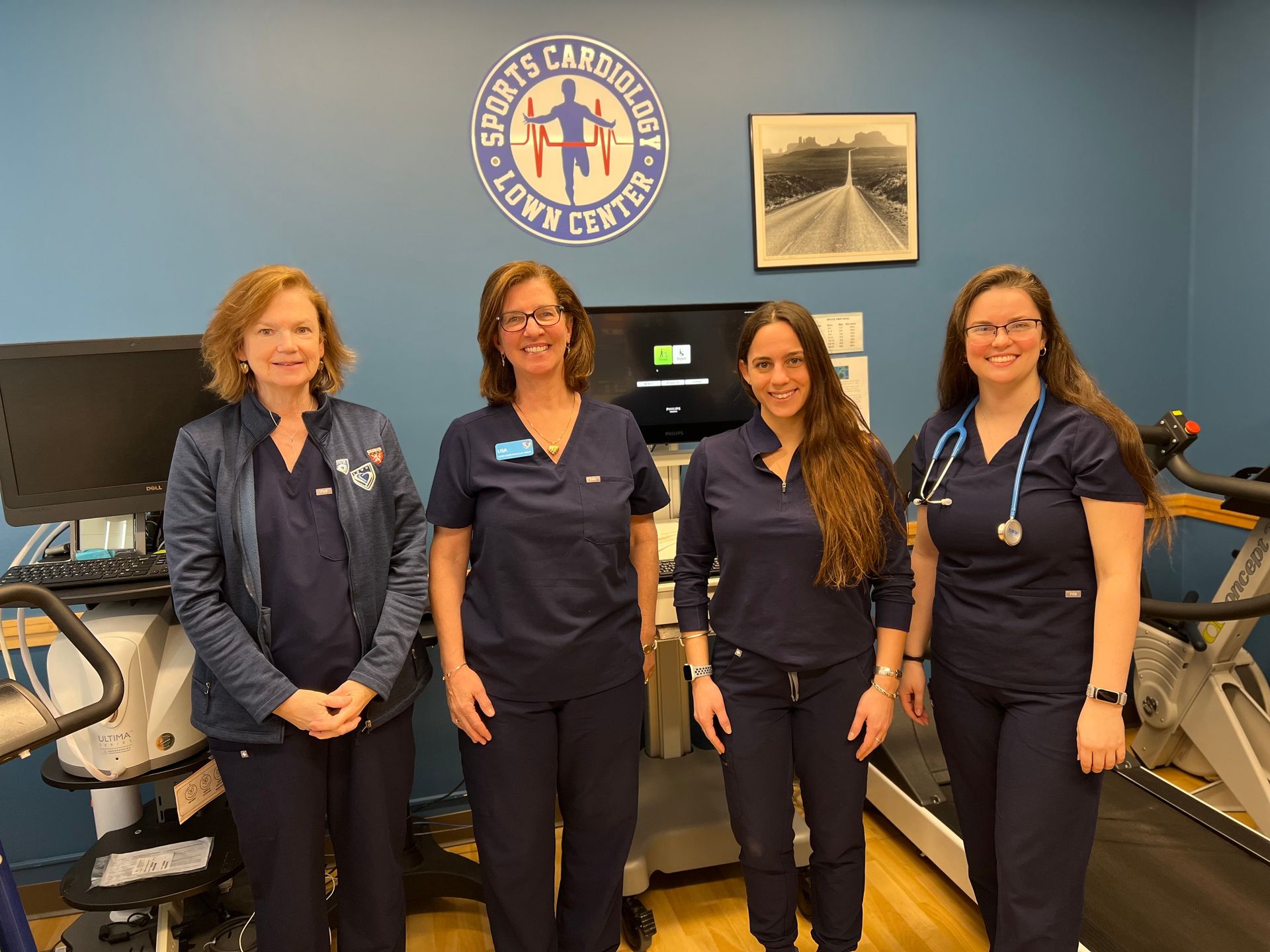 A group of women in scrubs are standing next to each other in a room with a treadmill.