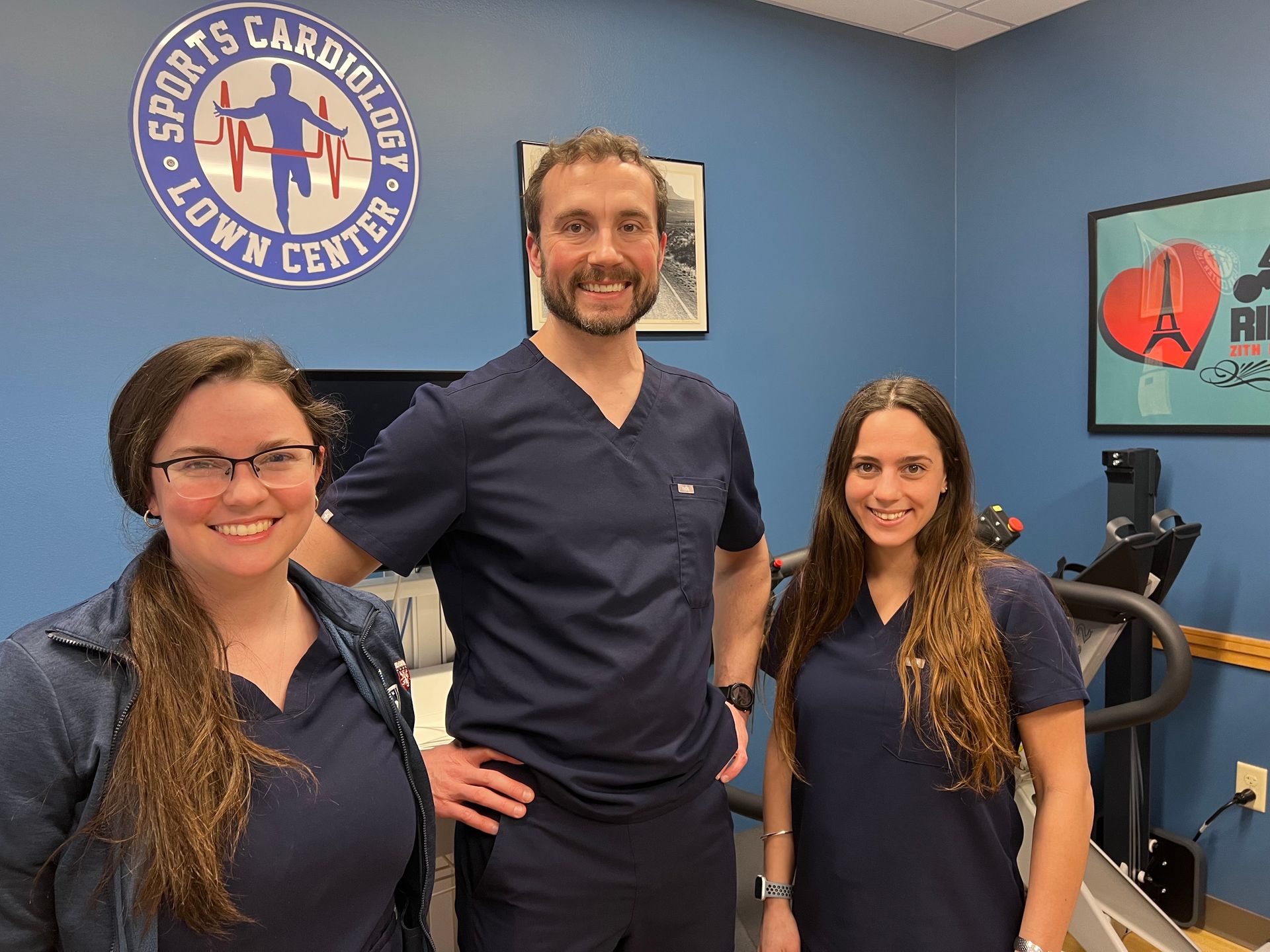 A man and two women are posing for a picture in a sports cardiologist office.