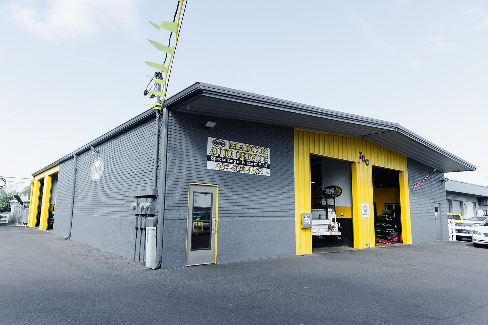Gray and yellow auto repair shop with open garage doors and a sign. | Marcos Auto Service