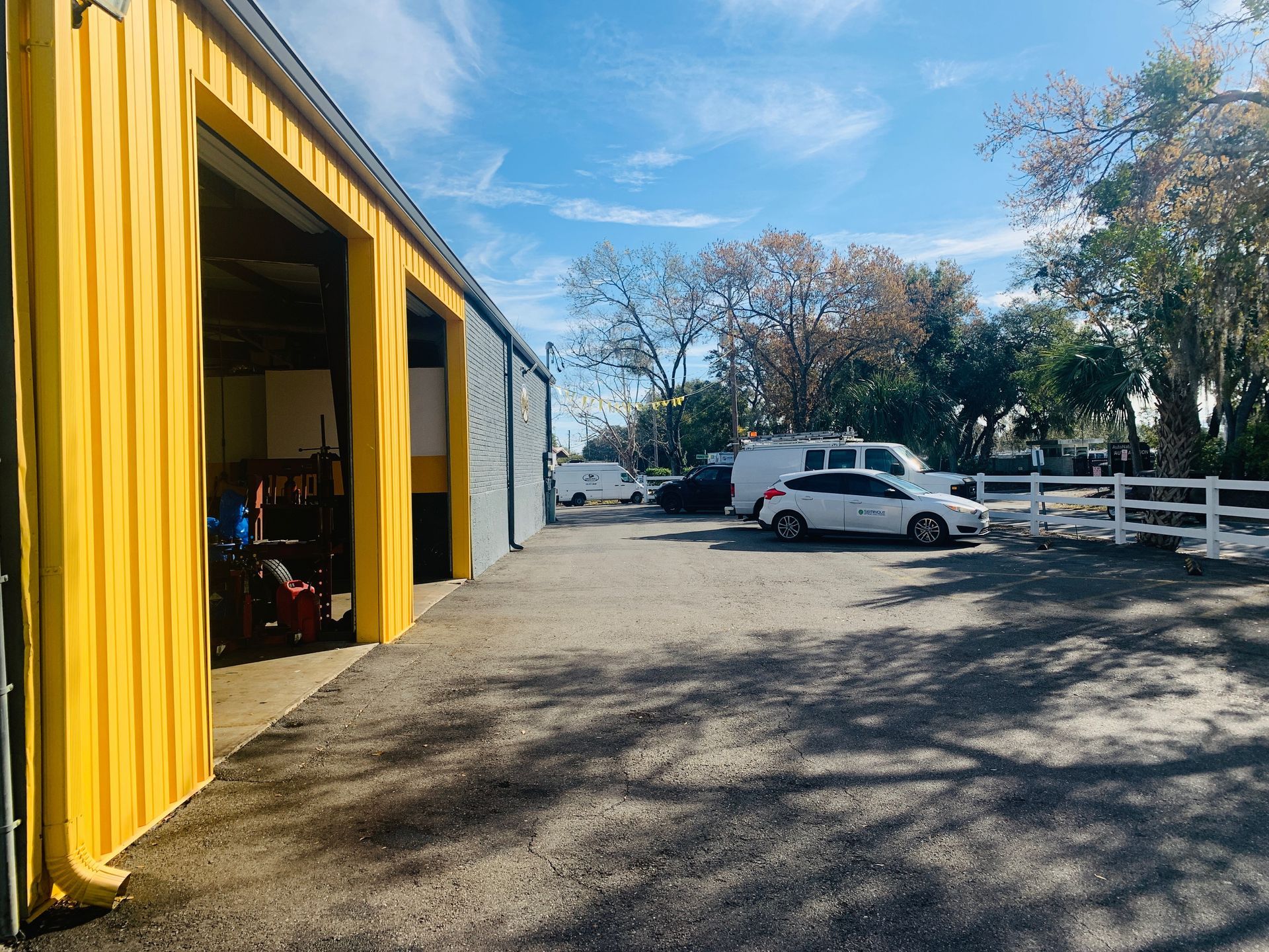 Yellow garage with open doors, gravel lot, and parked vehicles under a blue sky. | Marcos Auto Service