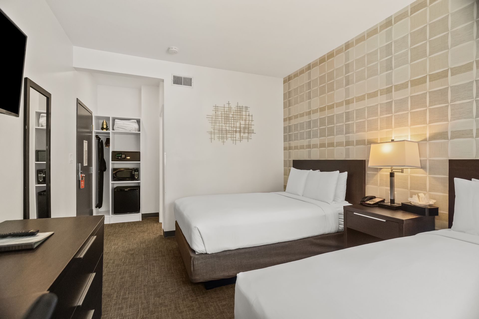 Modern hotel room with two beds, bedside lamps, a desk, and a patterned accent wall.