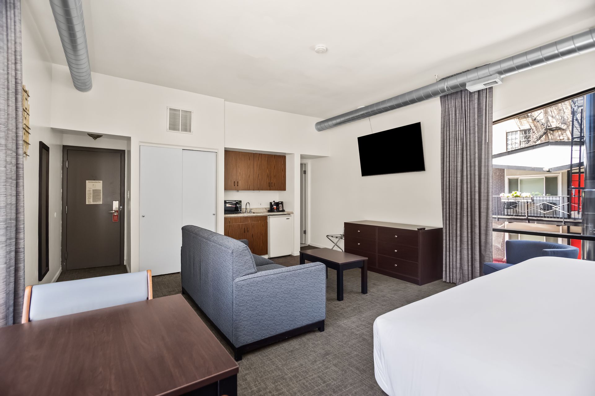 Hotel room with two beds, sofa, TV, and balcony view of a city street.