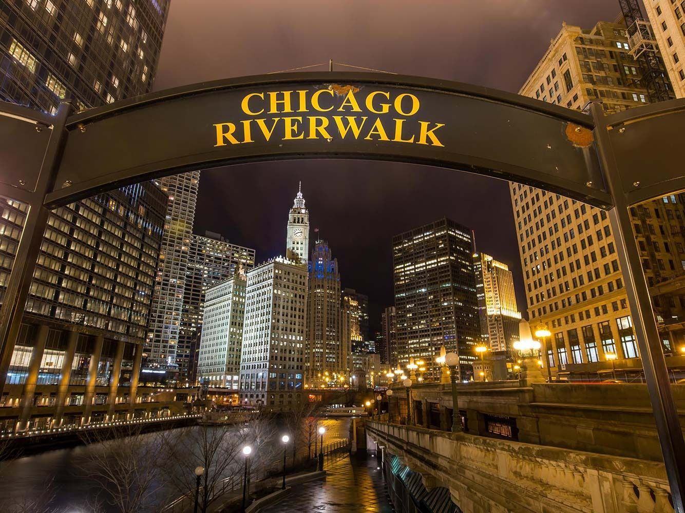Chicago Riverwalk sign with city skyline at night.