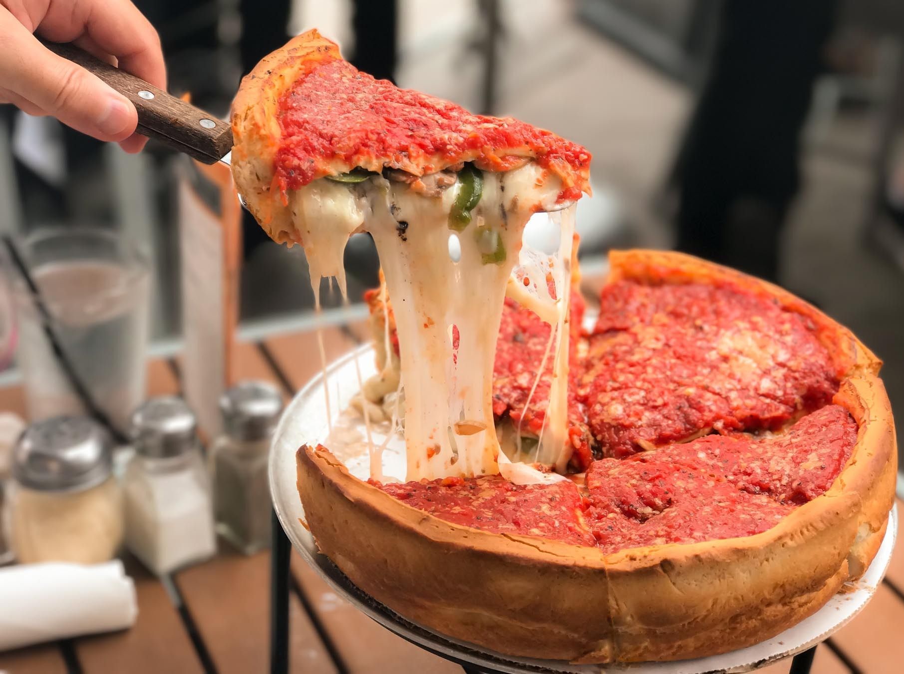 A slice of deep-dish pizza is lifted from a pie, with thick strings of melted cheese stretching over a restaurant table.