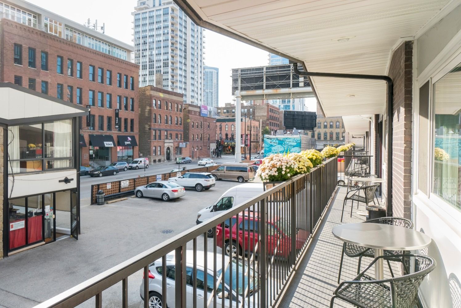 Balcony view overlooking a city street with parked cars, buildings, and a gas station.