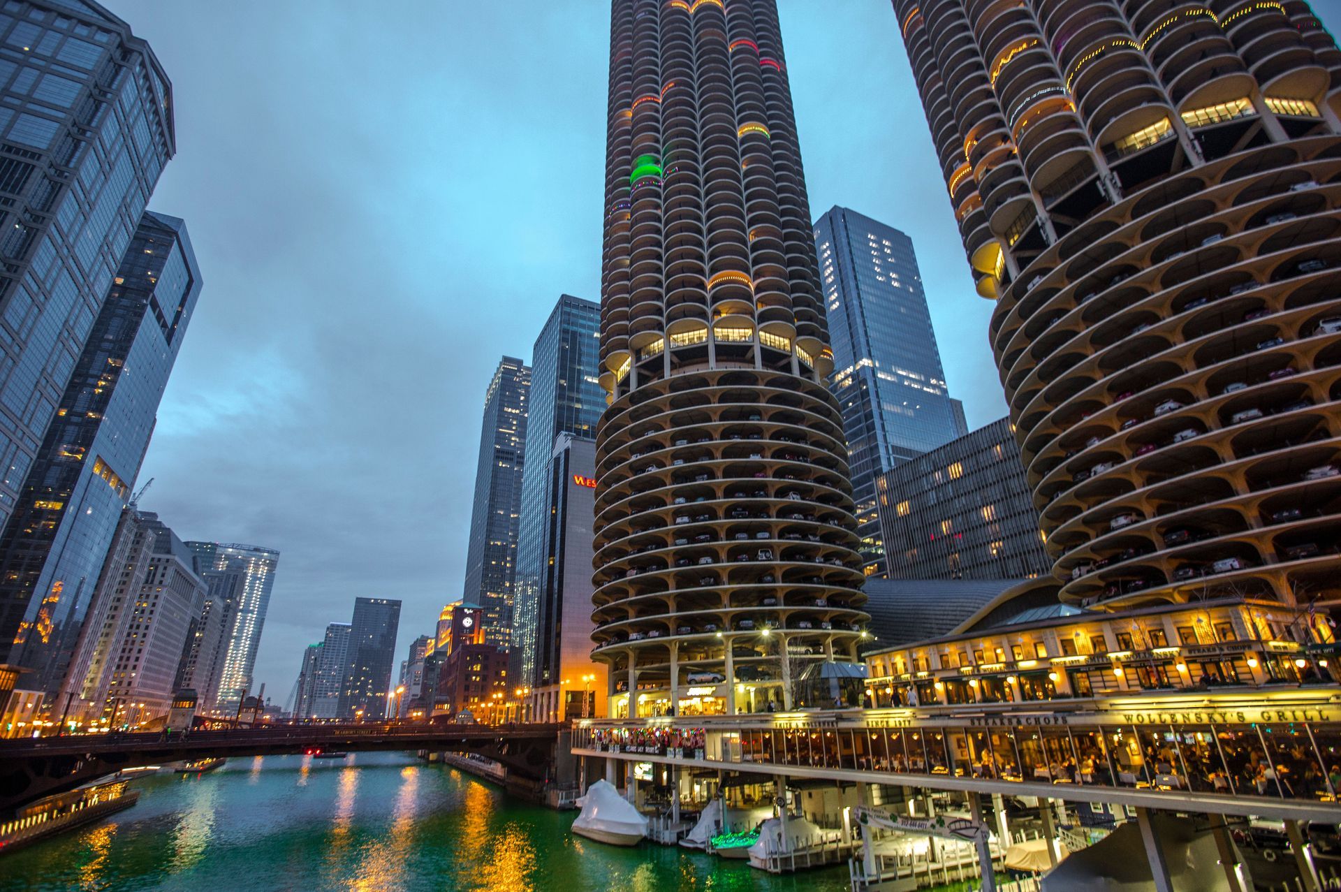 City skyline at dusk with illuminated high-rise towers and waterfront reflections along a river.