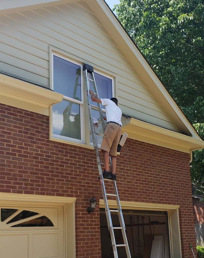 Person on a ladder cleaning a window on a brick house. Sunny day.